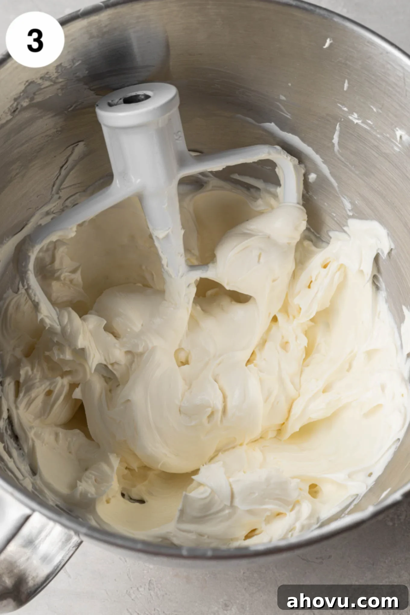 Creamy Cheesecake Squares 6 An overhead view of beaten cream cheese, sour cream, sugar, and vanilla in the bowl of a stand mixer, with a paddle attachment.