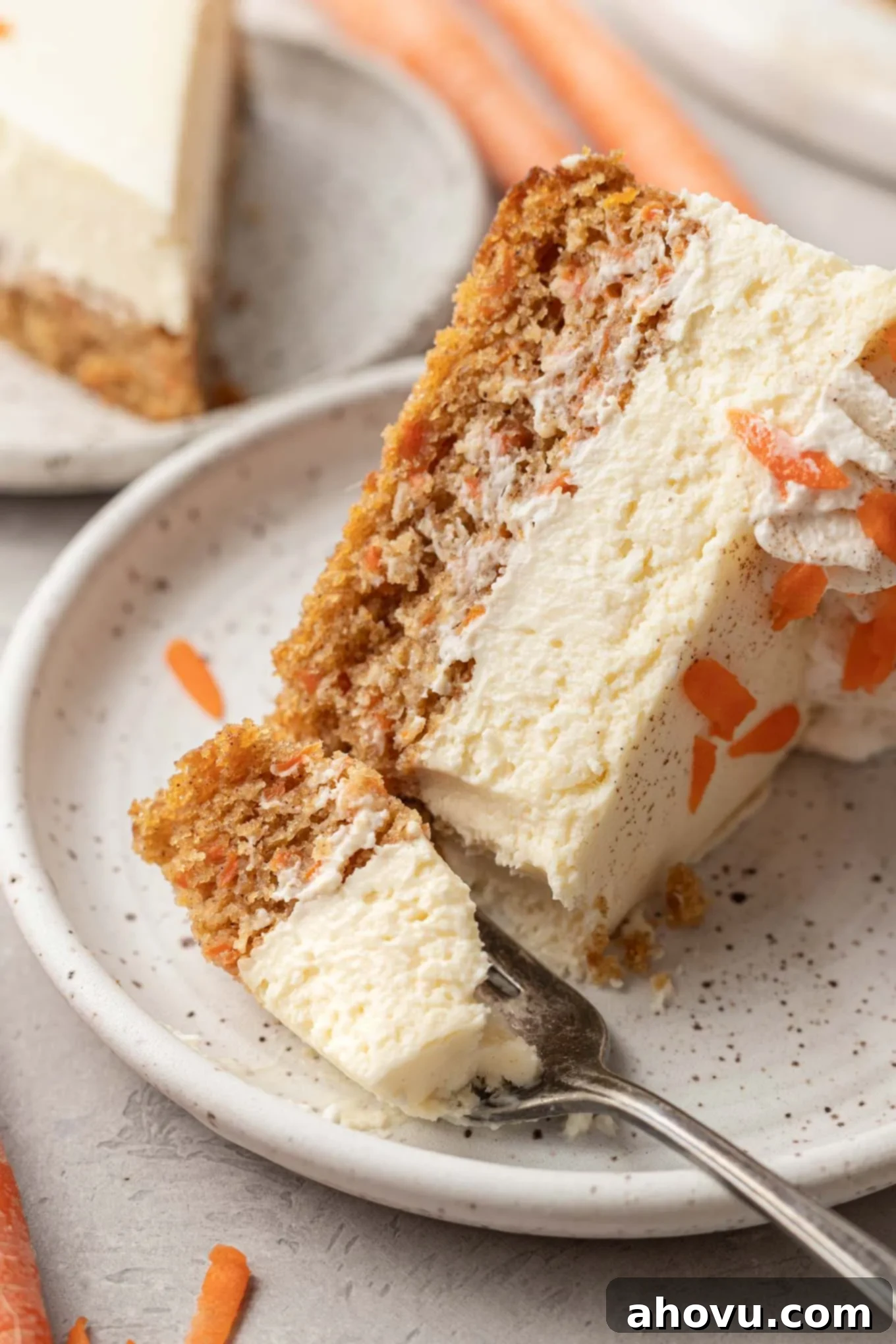 A perfectly plated slice of carrot cake cheesecake on a white dessert plate with a silver fork beside it.