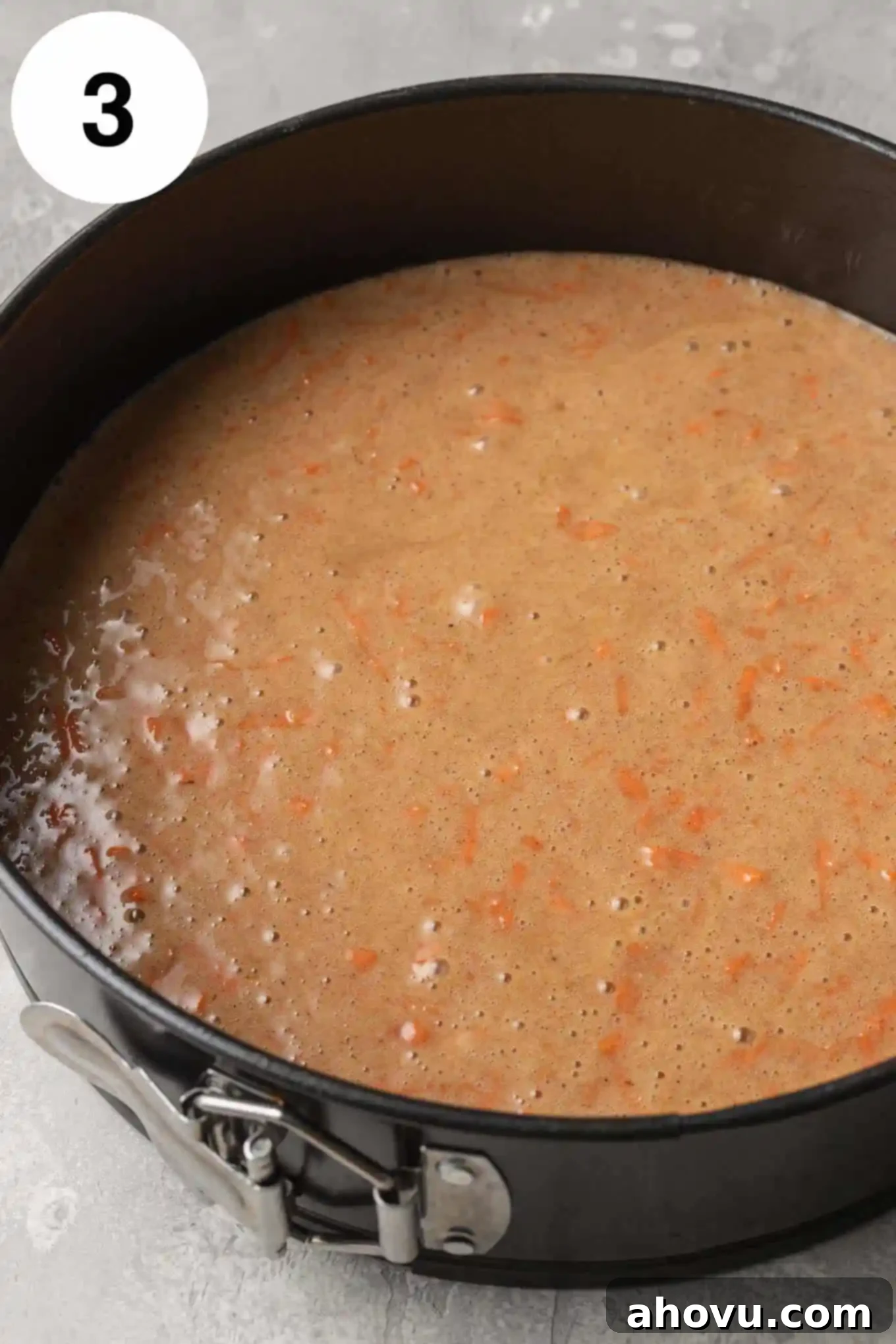 An overhead view of the raw carrot cake batter evenly spread in a prepared 9-inch springform pan.