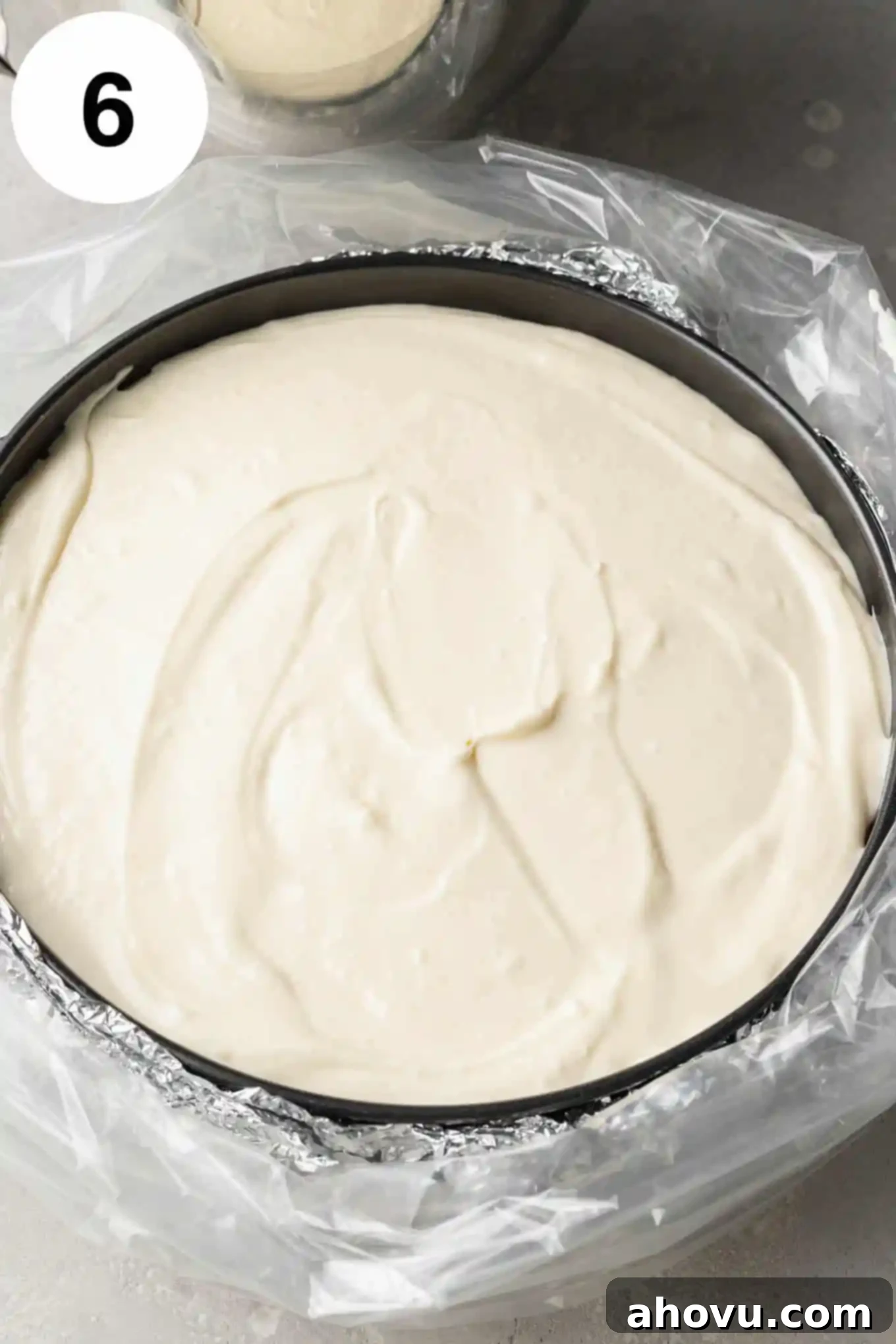 An overhead view of an unbaked carrot cake cheesecake in a springform pan, securely wrapped in aluminum foil and placed inside an oven bag for a water bath.