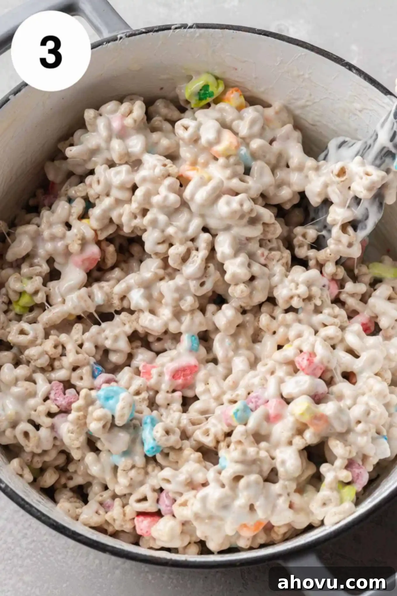 Lucky Charms Treats 6 An overhead view of Lucky Charms cereal being gently folded into the gooey marshmallow mixture in a large saucepan.