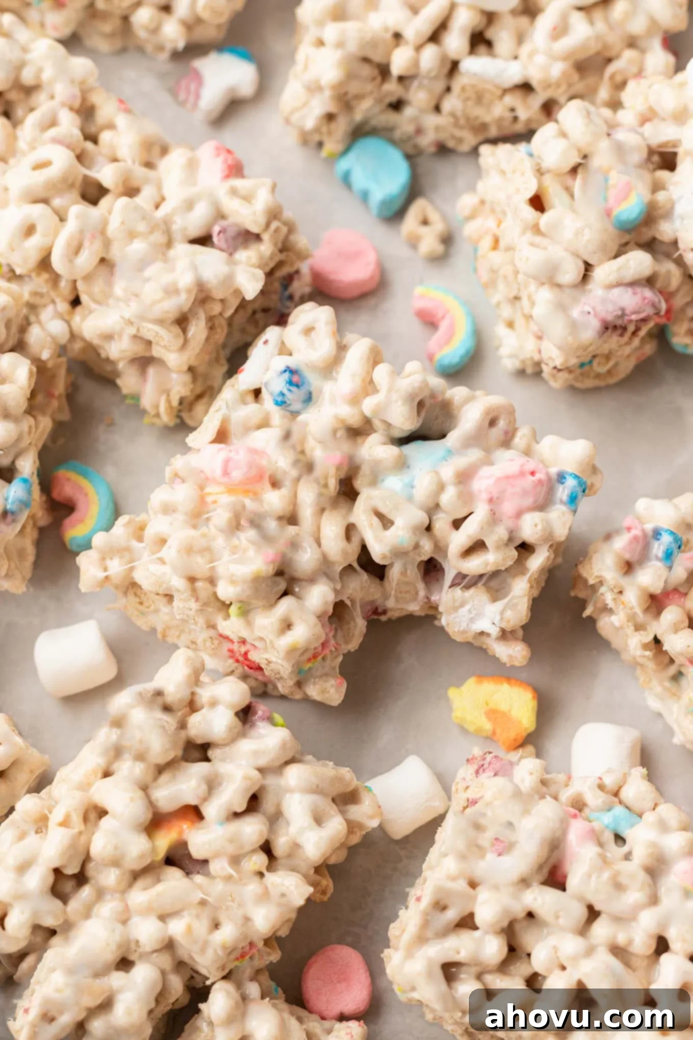 Lucky Charms Treats 9 A close-up of a Lucky Charms treat with a bite taken out, showing the chewy interior. It's surrounded by more delicious bars on a wooden surface.