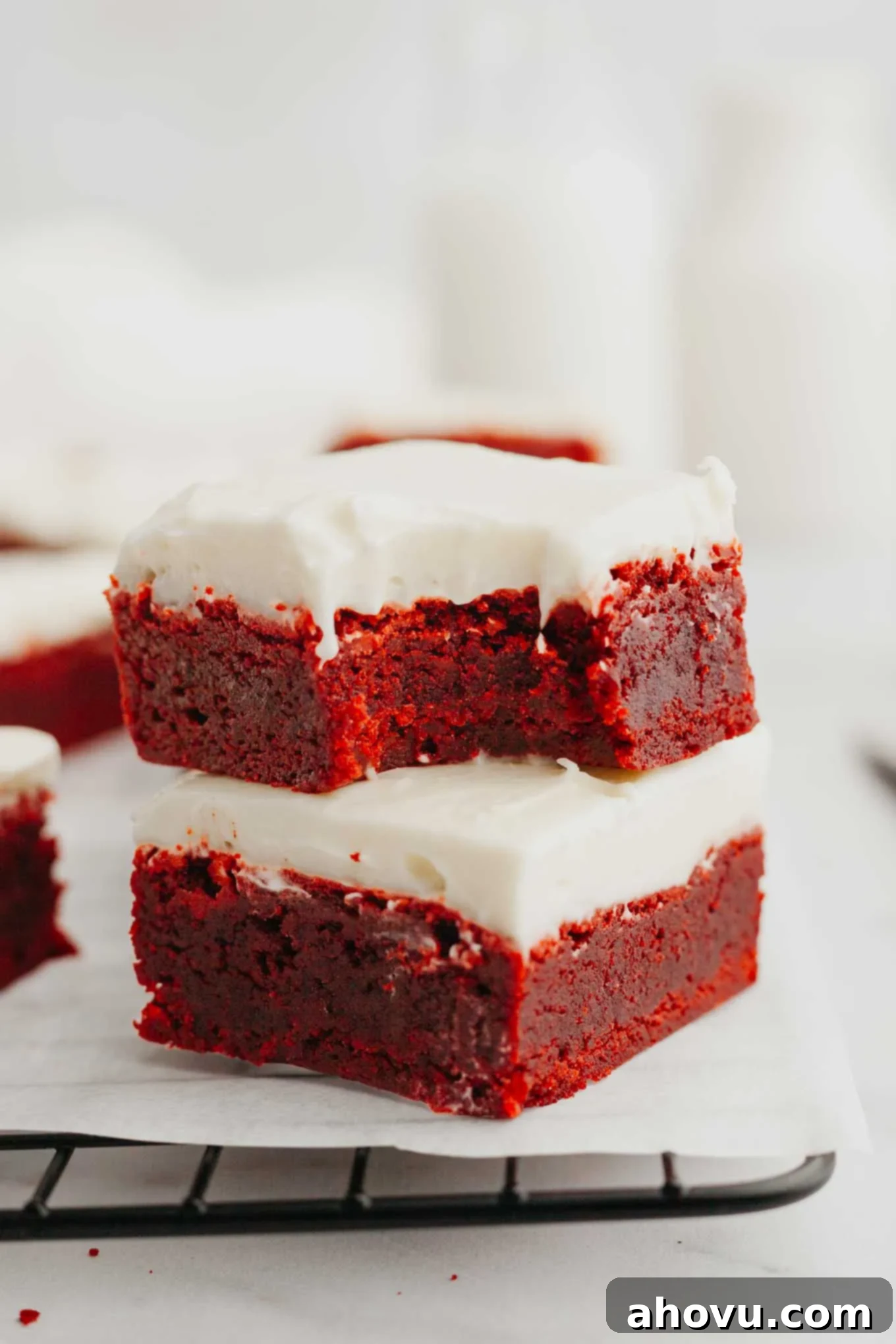 Two red velvet brownies stacked on top of each other; the top one has a bite missing. 