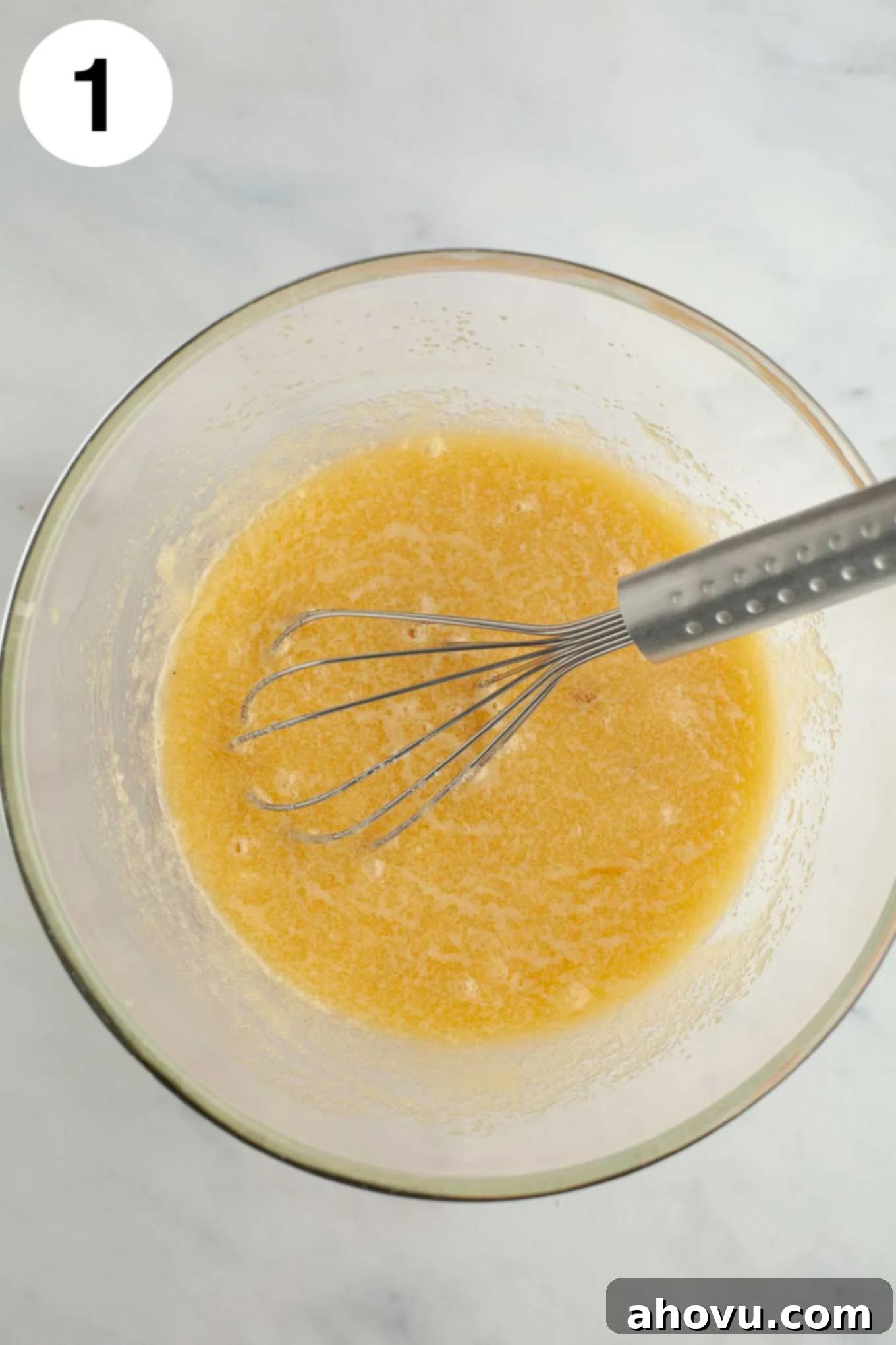 Melted butter and sugar whisked together in a glass mixing bowl.