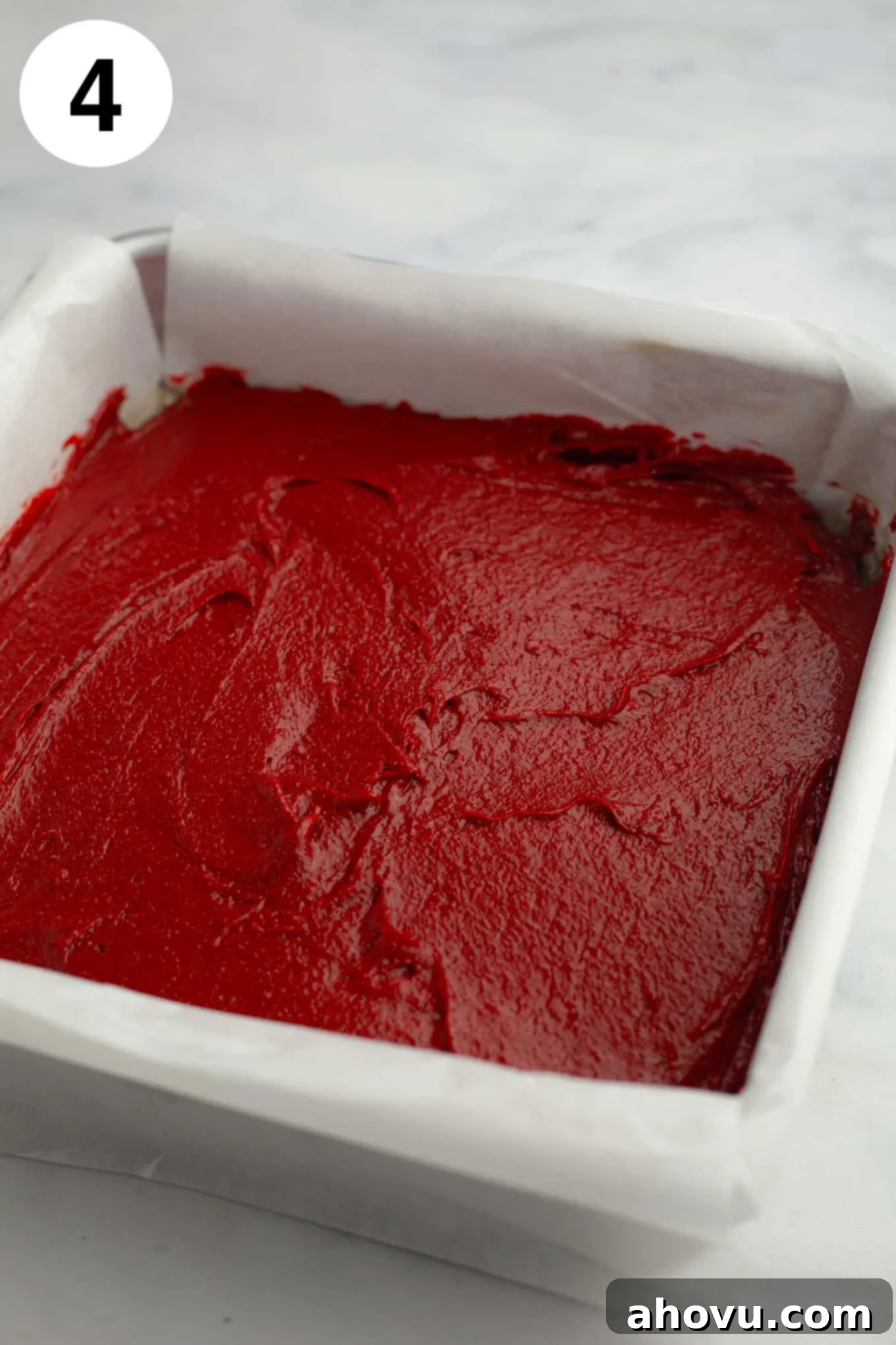 Red velvet brownie batter smoothed out into a parchment paper lined baking pan.