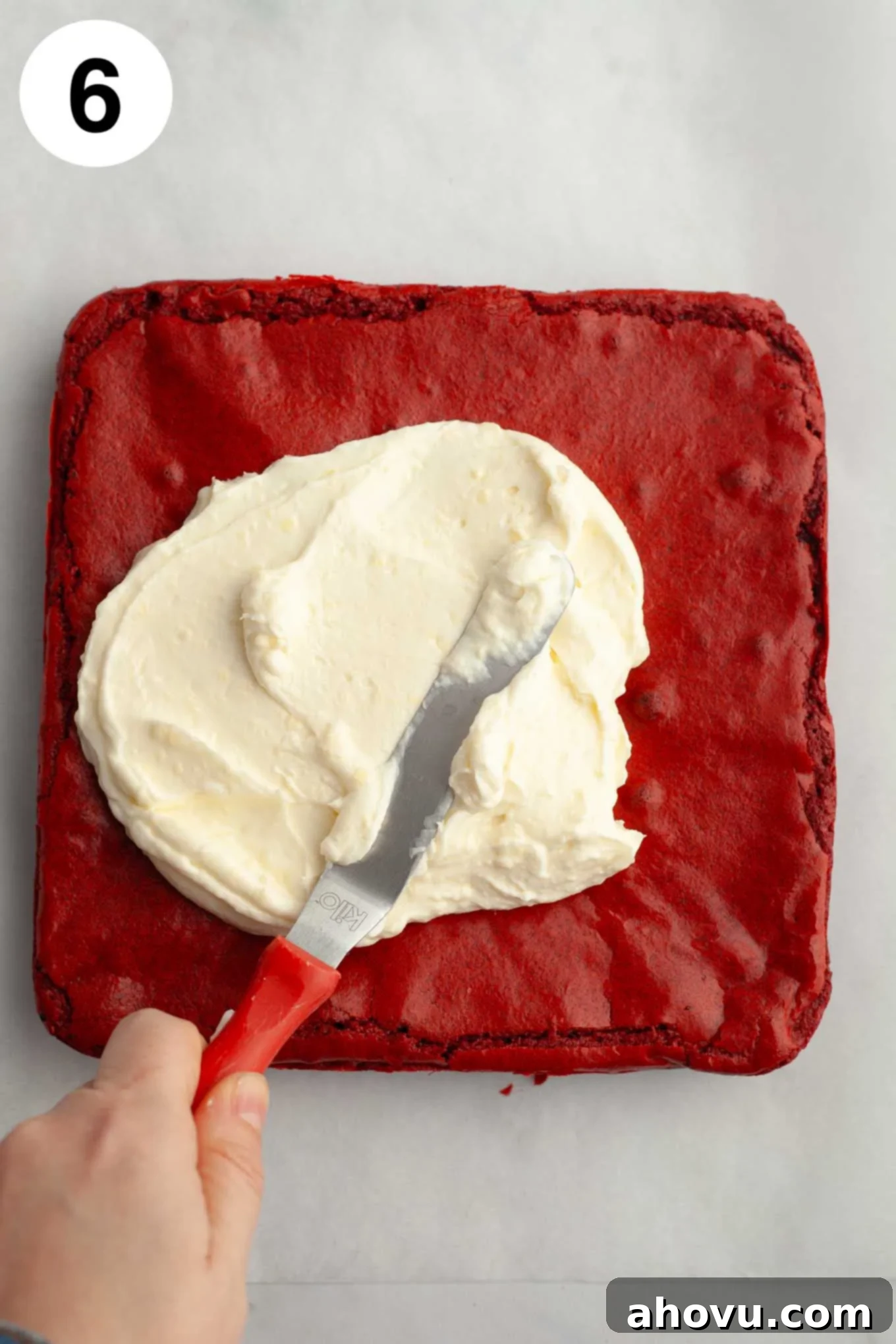 An overhead view of cream cheese icing being spread on top of the brownies with an angled spatula.