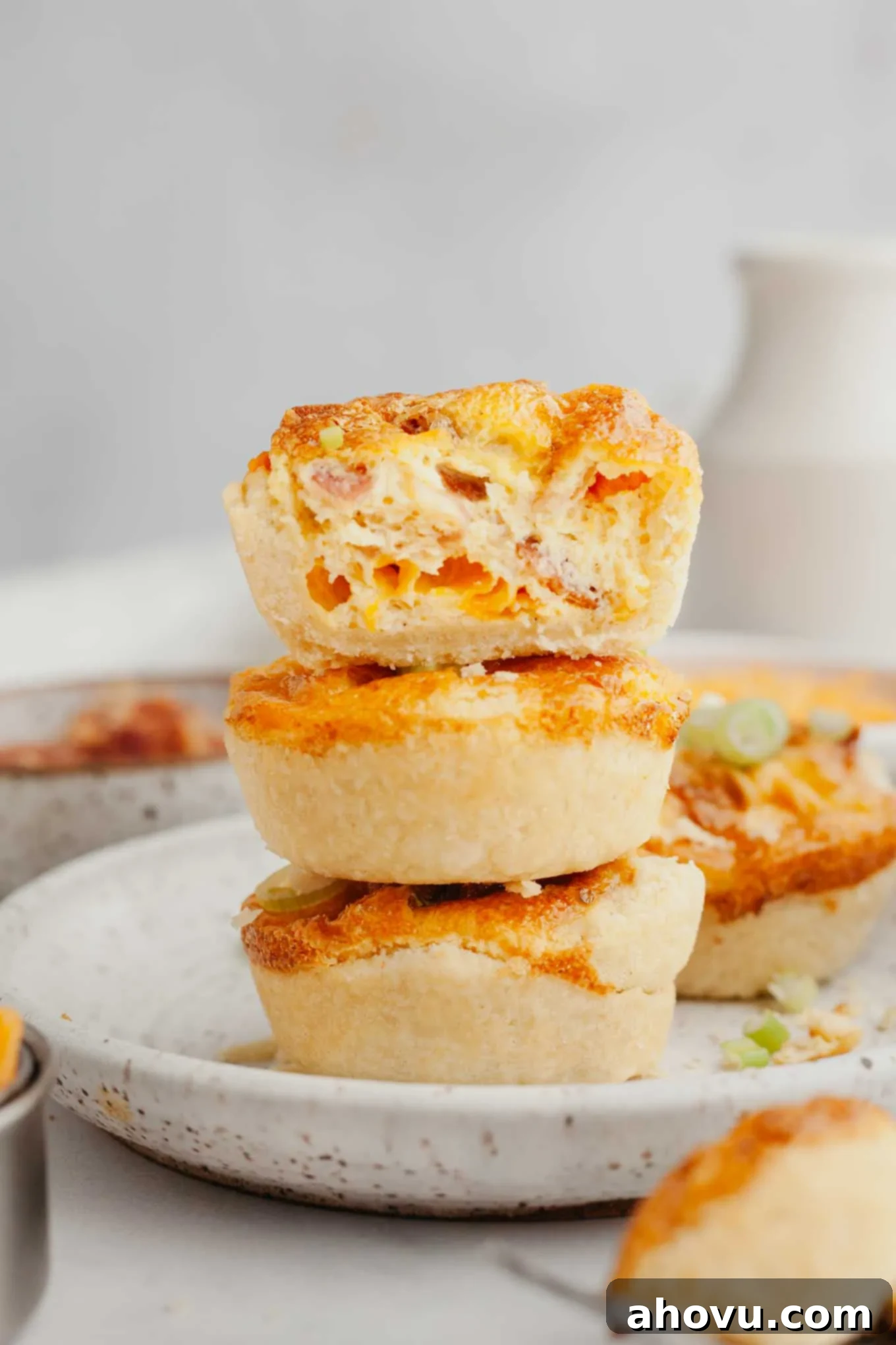 A stack of three perfectly baked bite-sized quiches presented on a speckled white plate, highlighting their golden crusts and inviting filling.