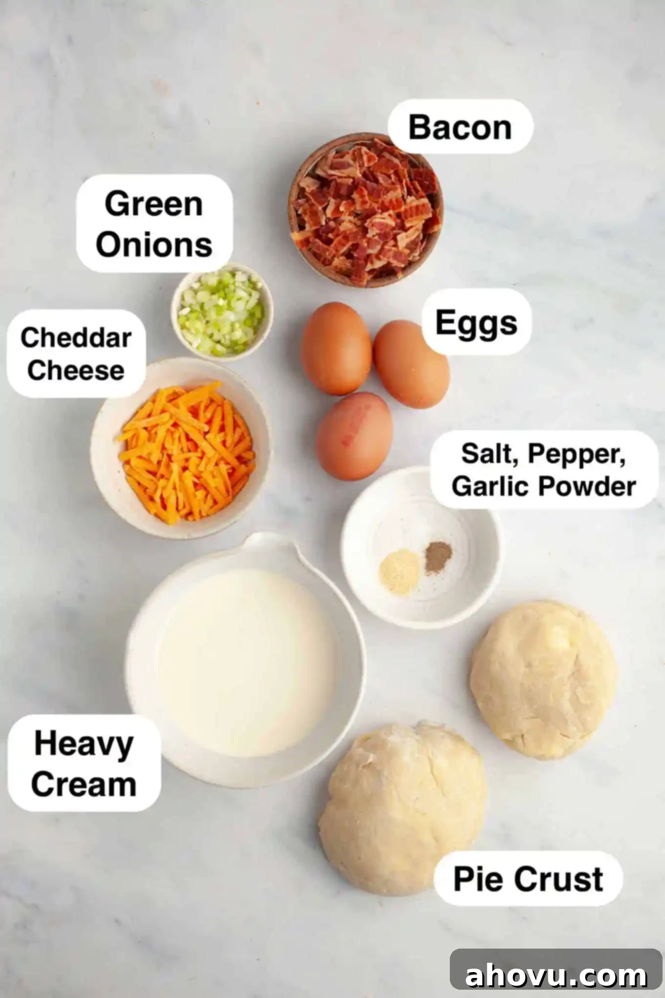 An overhead view of the ingredients laid out on a kitchen counter, ready to be prepared for mini breakfast quiche. This includes eggs, cream, bacon, cheese, and green onions.