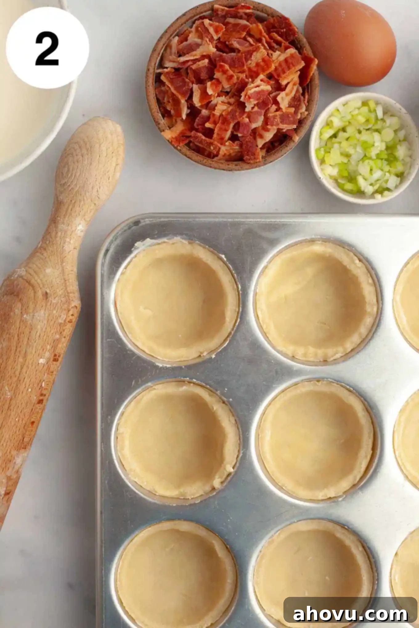 An overhead view of mini quiche crusts perfectly pressed into the individual cups of a muffin pan, showcasing preparation before filling.