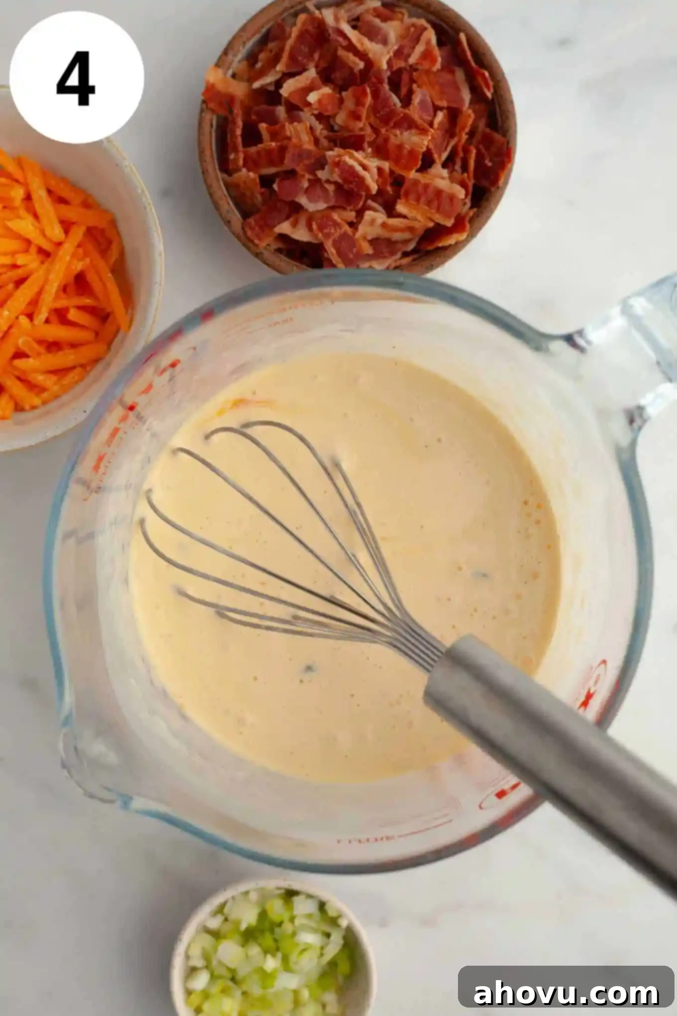 An overhead view of the completed mini quiche filling, a creamy egg mixture, in a glass measuring cup, ready to be poured into the crusts.