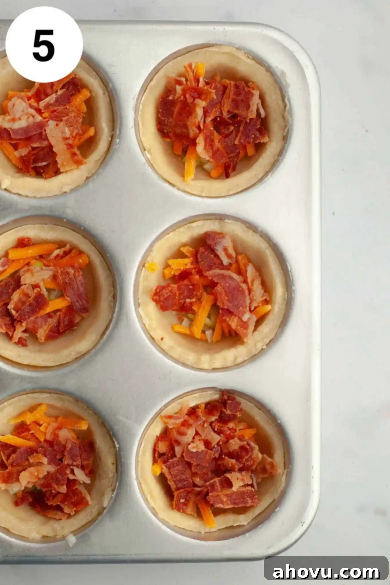 An overhead view of a muffin pan with partially filled mini quiches, showing the initial layer of mix-ins before the egg mixture is added.