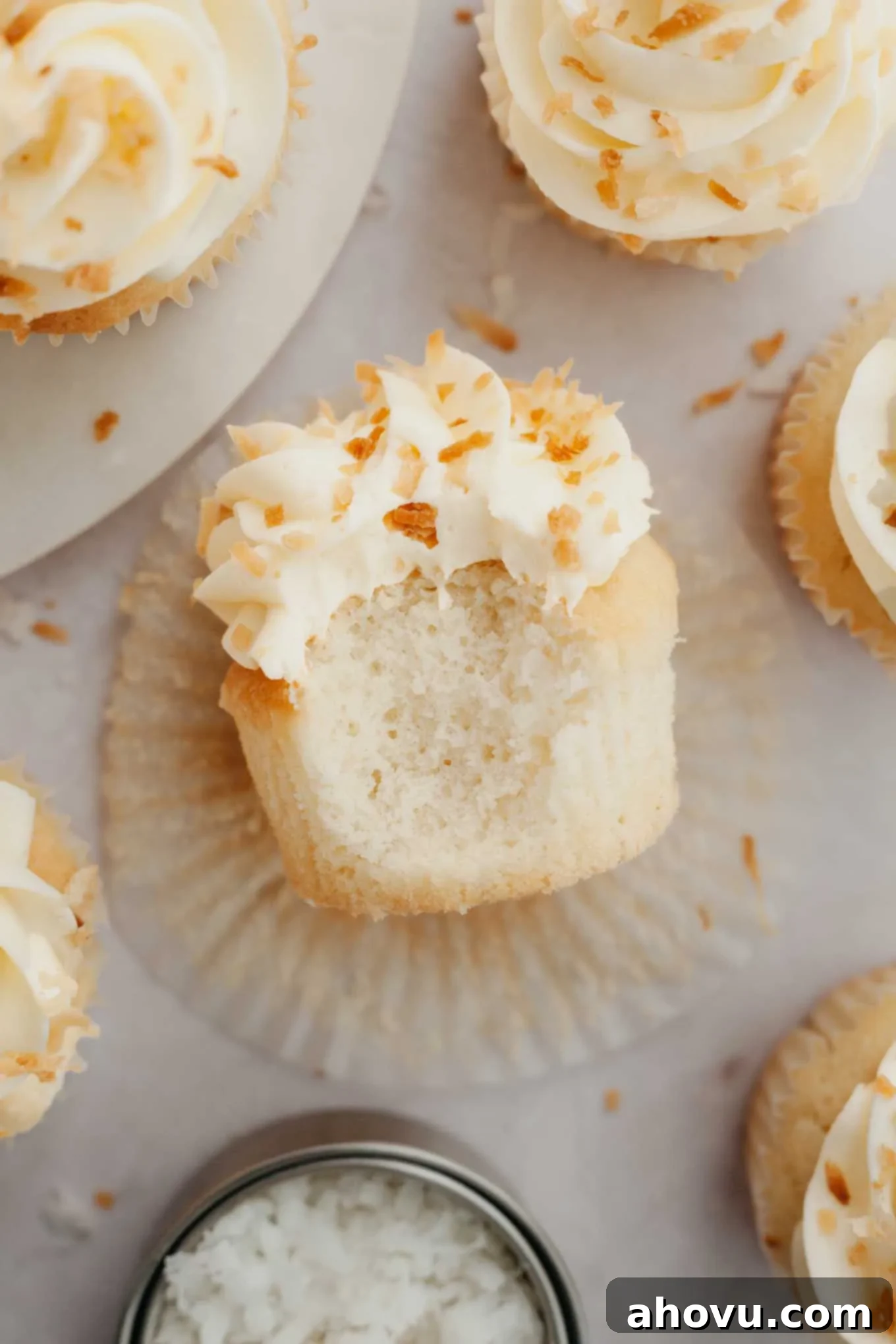 An overhead view of a coconut cupcake, beautifully frosted and garnished, lying on its side, inviting a closer look.