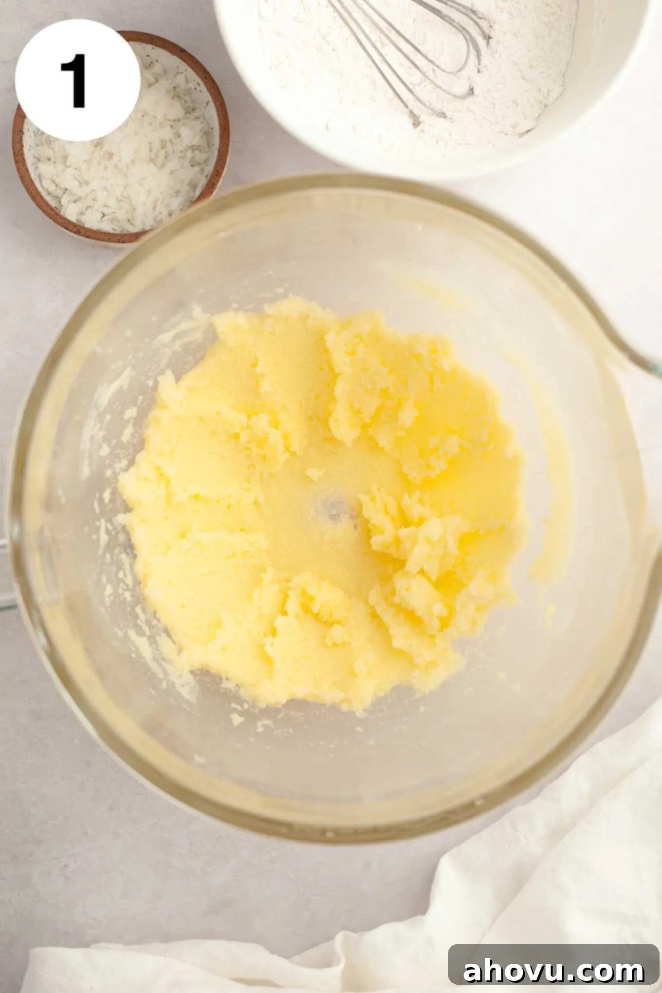 An overhead view of softened butter and granulated sugar being creamed together in a glass mixing bowl.