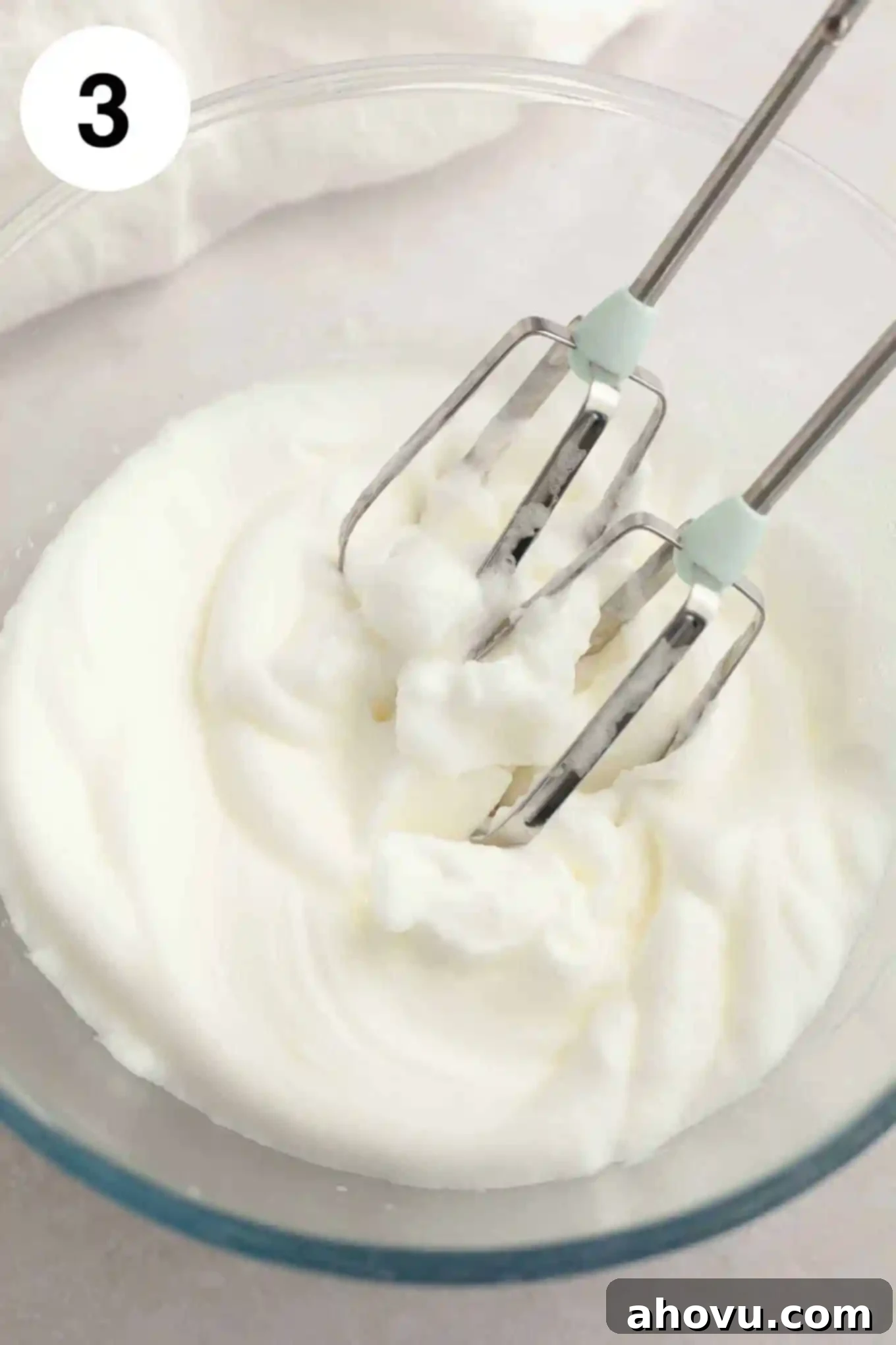 An overhead view of stiffly whipped egg whites in a clean glass mixing bowl, ready to be folded into the cupcake batter.