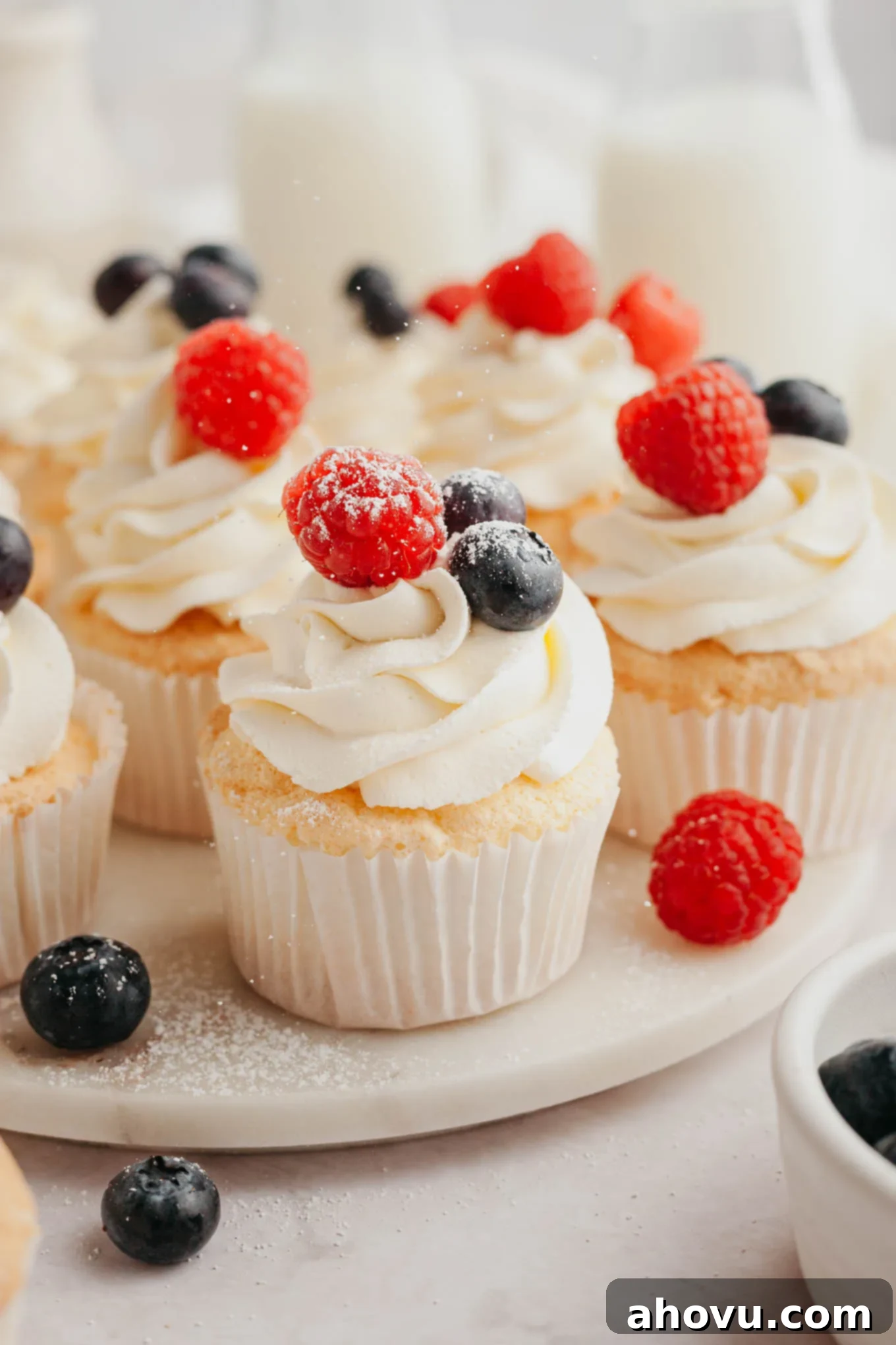 Angel food cupcakes topped with whipped cream and fresh berries, arranged beautifully on a serving plate.