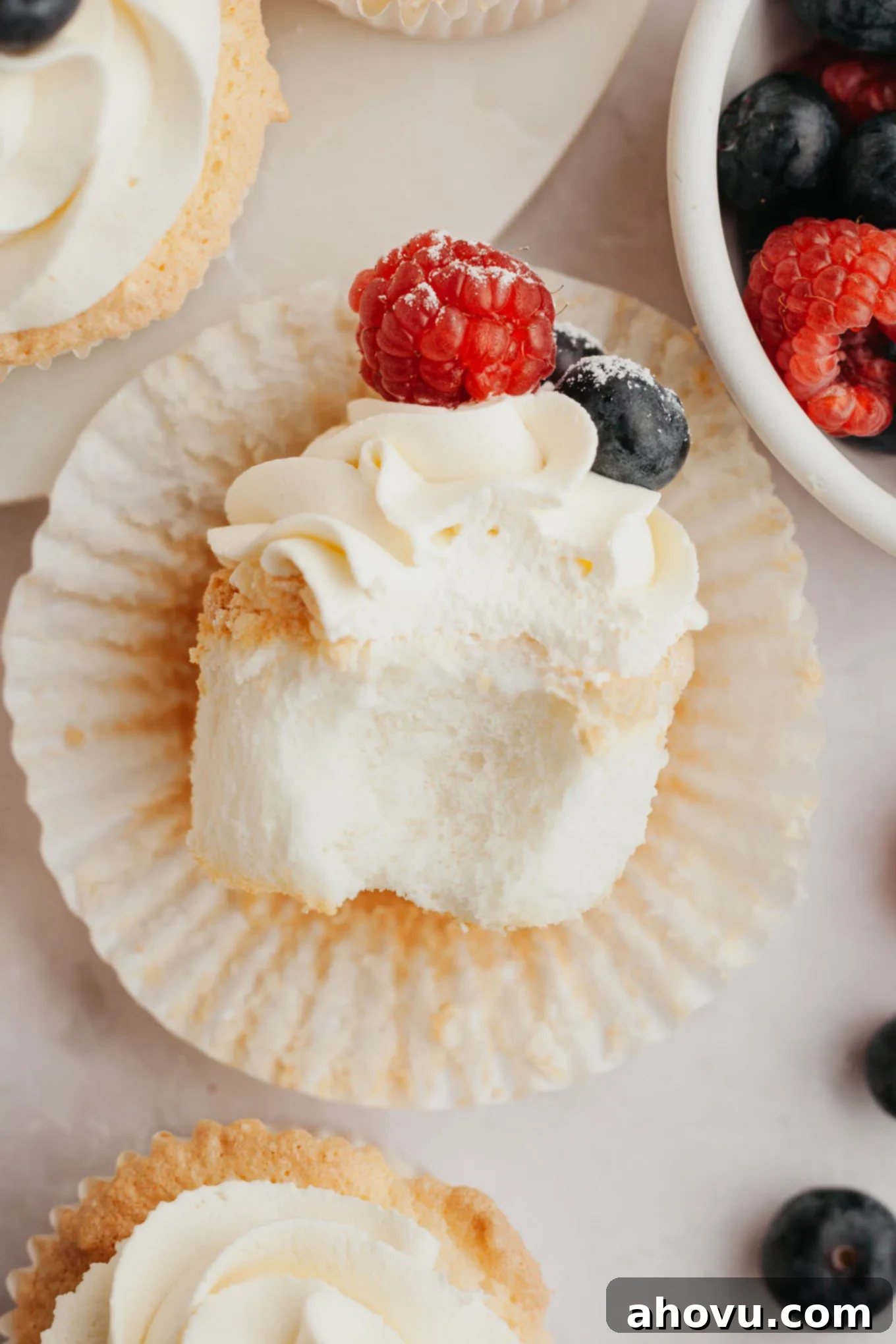 An overhead view of an angel food cupcake, with a bite taken out, resting on its side to reveal its soft, spongy interior.