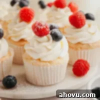 Several angel food cupcakes topped with whipped cream and fresh berries on a marble serving platter.
