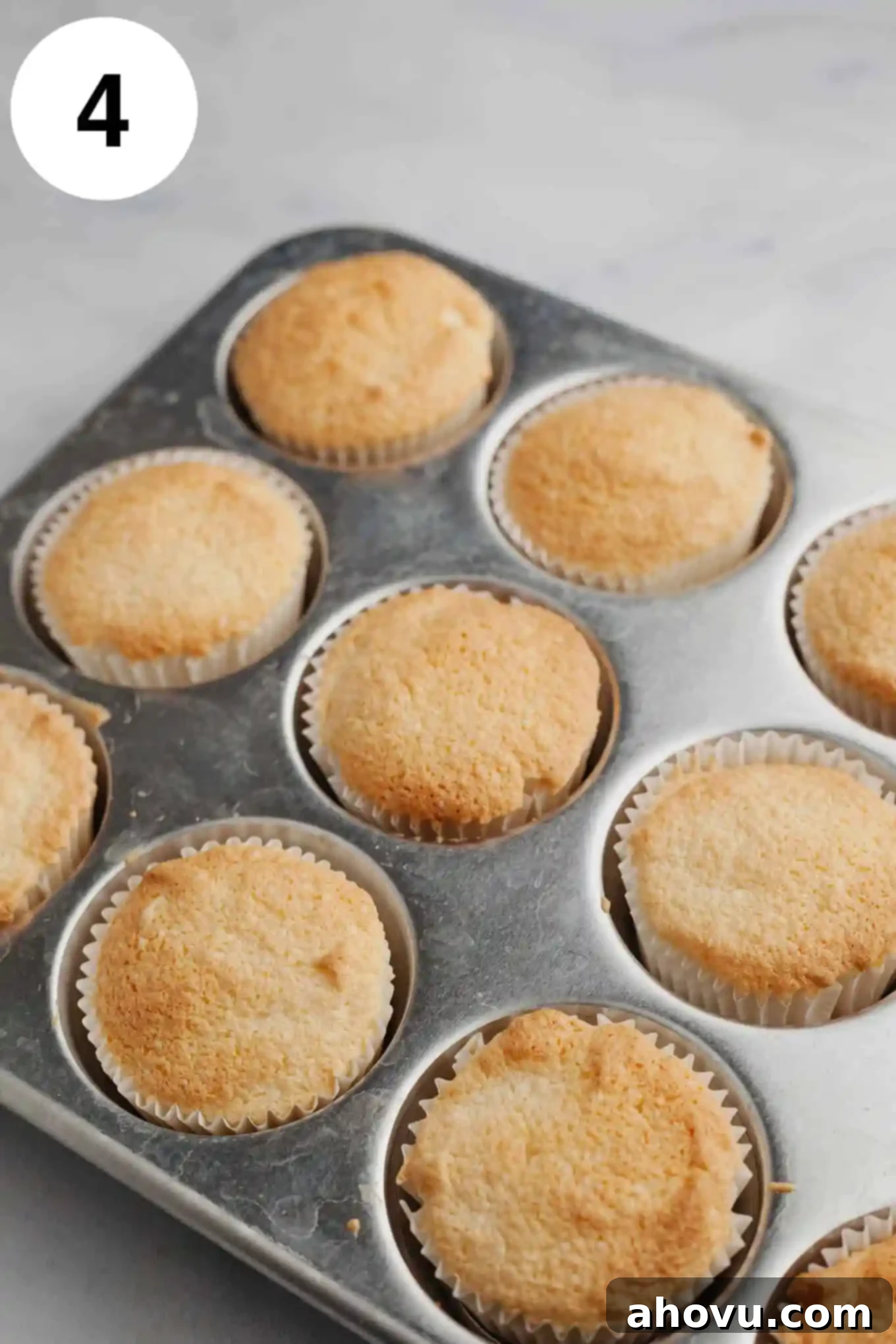 A tray of unfrosted, perfectly golden-brown angel food cupcakes nestled in their liners, freshly baked in a cupcake pan.