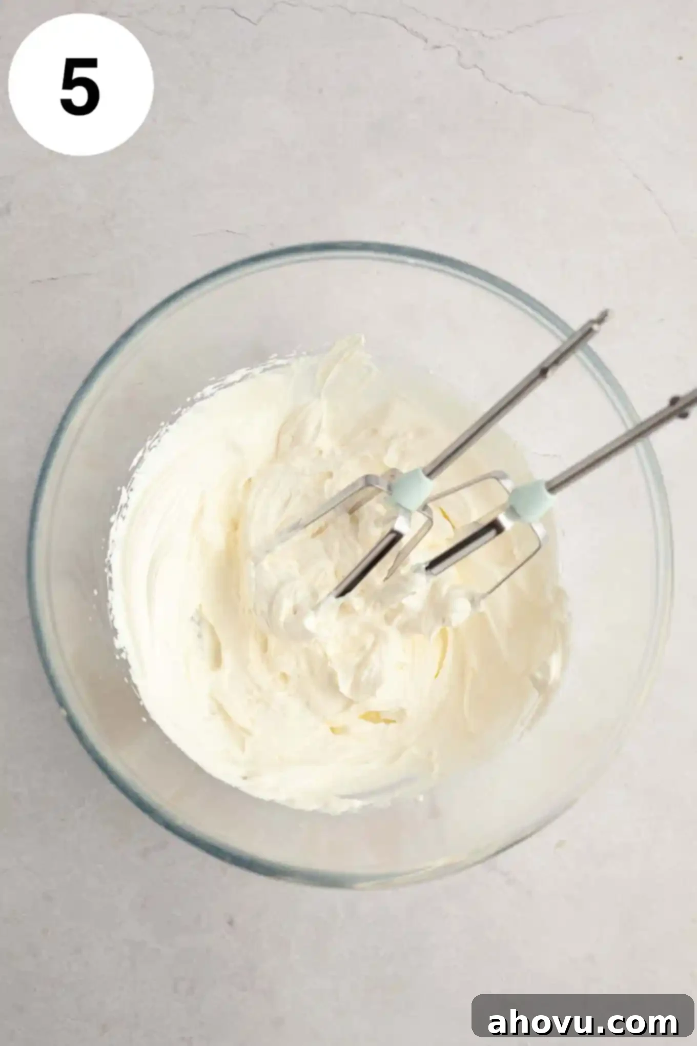 Thick, perfectly whipped cream beaten to stiff peaks, ready for frosting, presented in a clear glass mixing bowl.