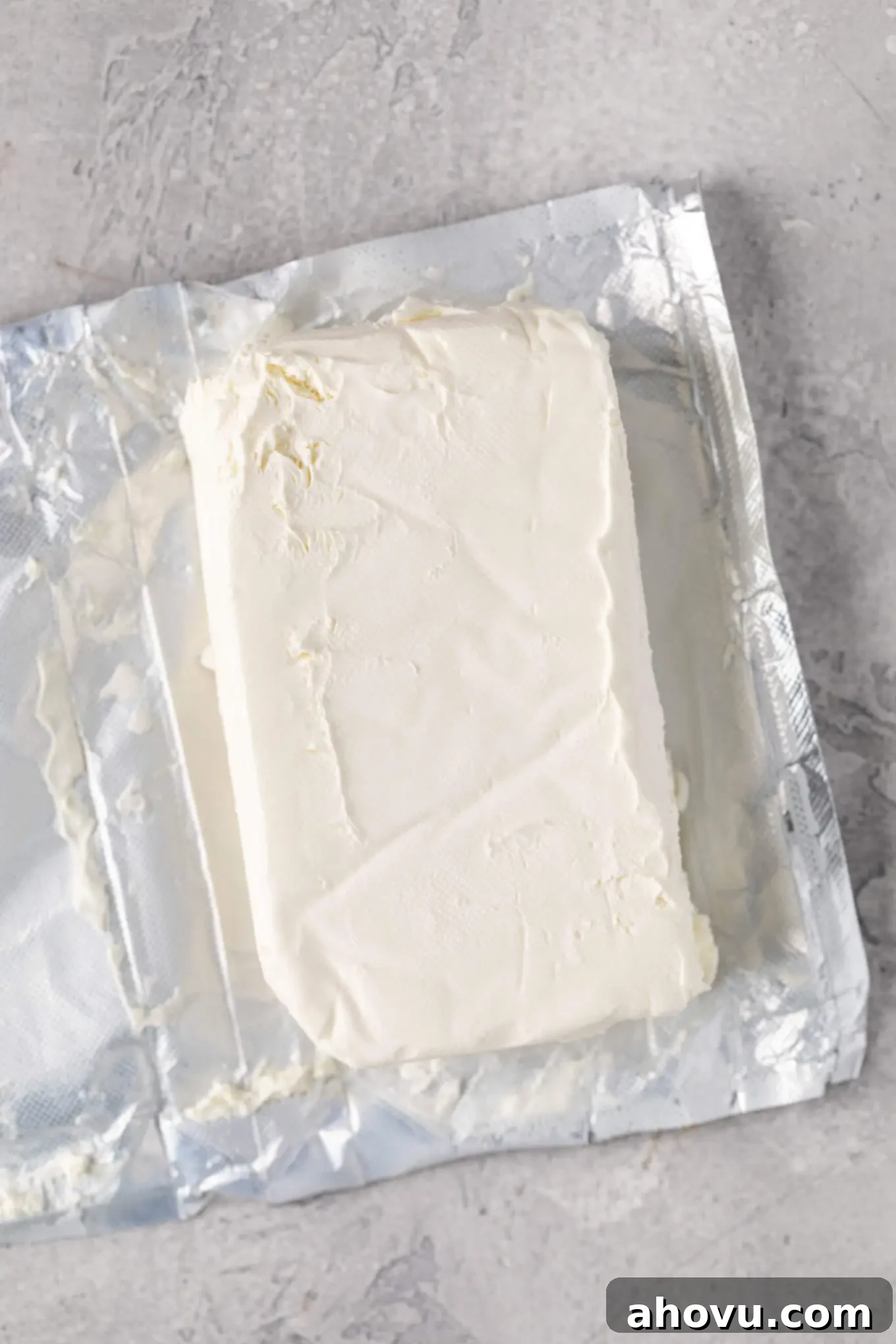 An overhead view of an opened package of brick-style cream cheese, showing its firm texture before softening.