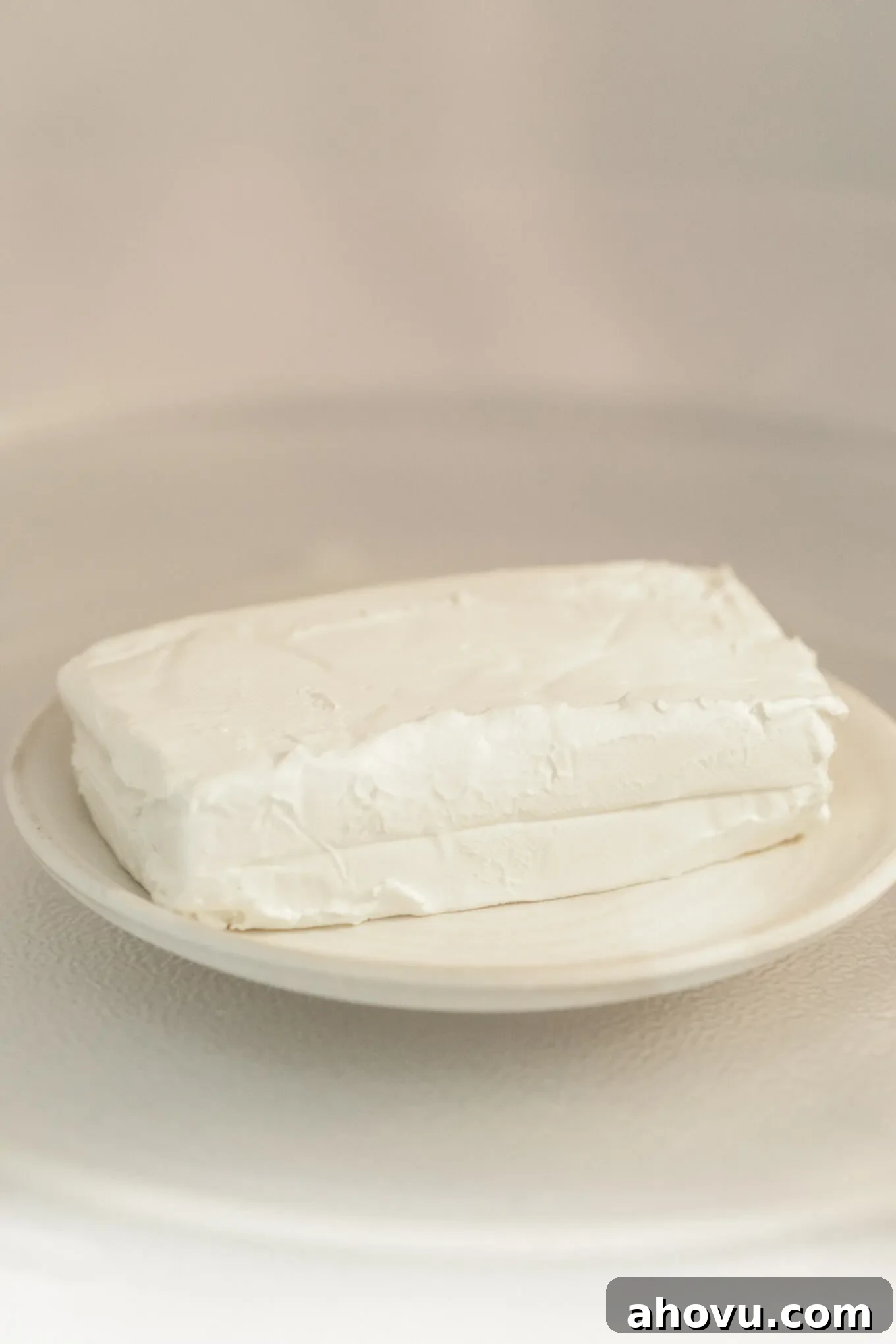 A plate with a block of cream cheese sitting inside of a microwave, illustrating the fastest softening technique with caution.