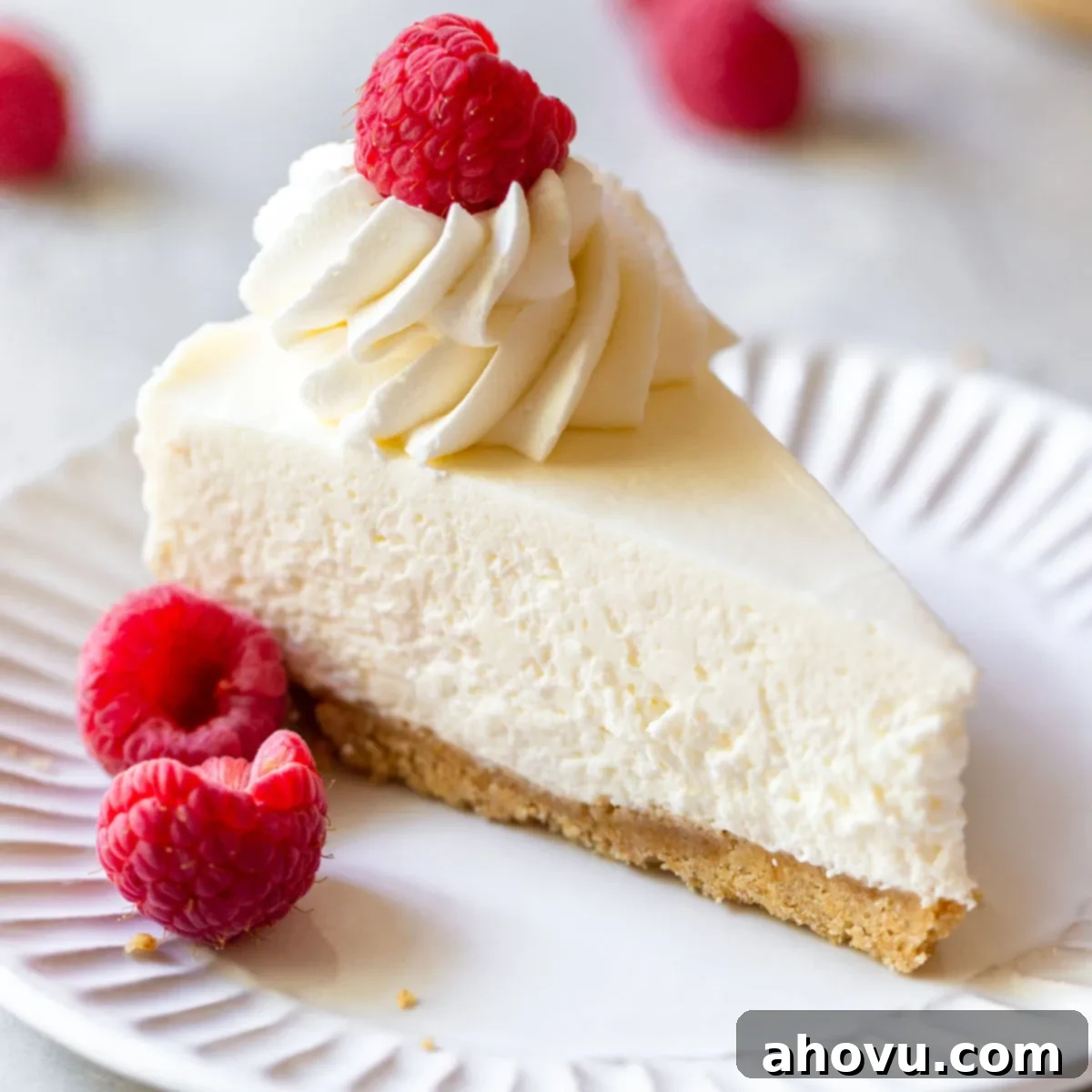 A single slice of no-bake cheesecake on a white plate topped generously with whipped cream and vibrant fresh raspberries, showcasing a delicious use for cream cheese.