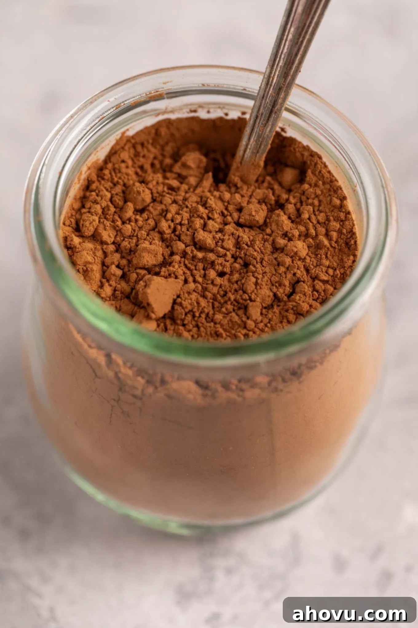 A small glass jar filled with cocoa powder. A spoon is resting inside of the jar.
