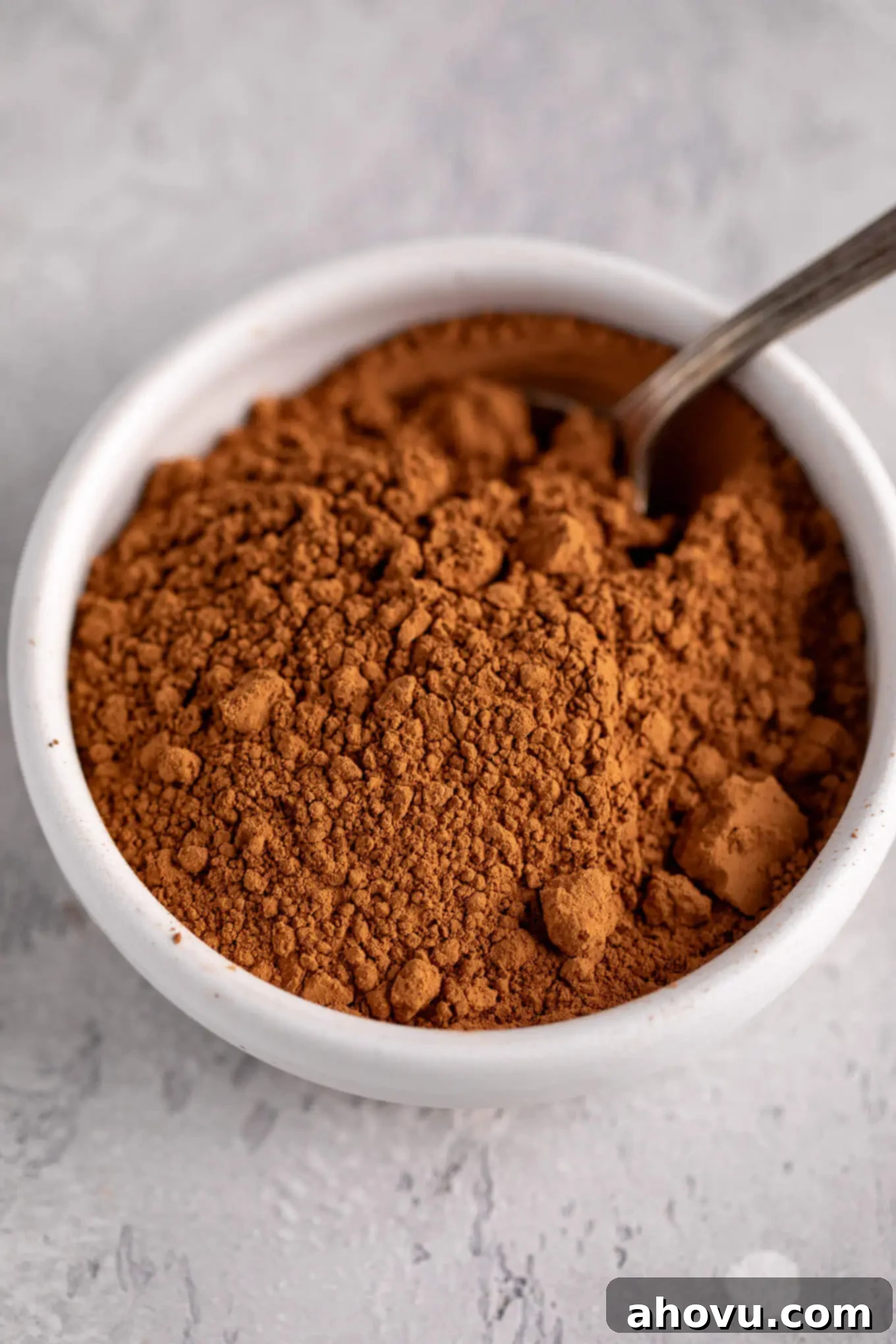 Natural cocoa powder inside of a white bowl with a spoon inside of it.