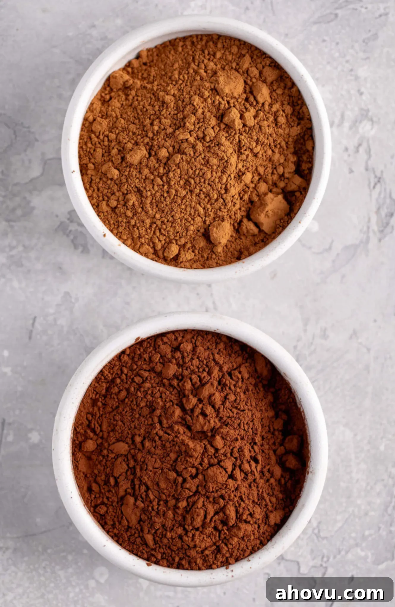 An overhead image of a white bowl filled with natural cocoa powder and another white bowl filled with Dutch process cocoa powder.