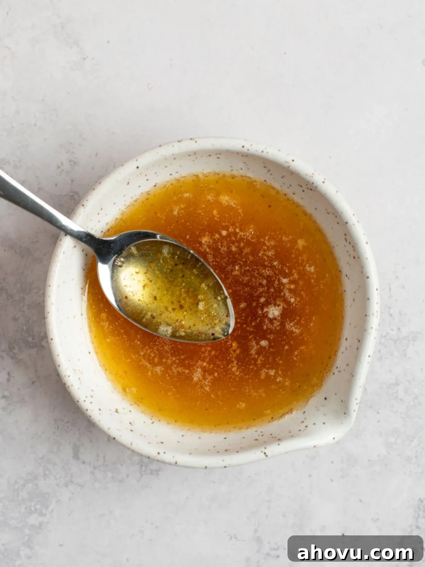 The Art of Brown Butter 8 A small, speckled white bowl filled with golden brown butter, featuring a spoon resting inside, ready for use.