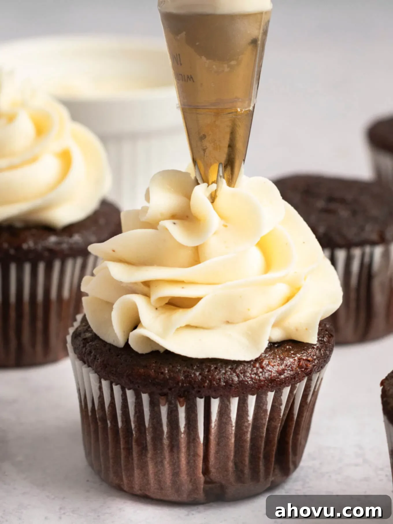 A skilled hand expertly piping creamy brown butter frosting onto a freshly baked chocolate cupcake, creating an elegant swirl.