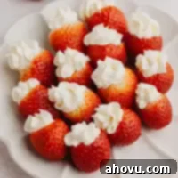 Strawberry Cheesecake Poppers 11 Several beautifully arranged cheesecake stuffed strawberries on a white scalloped plate, glistening with freshness.