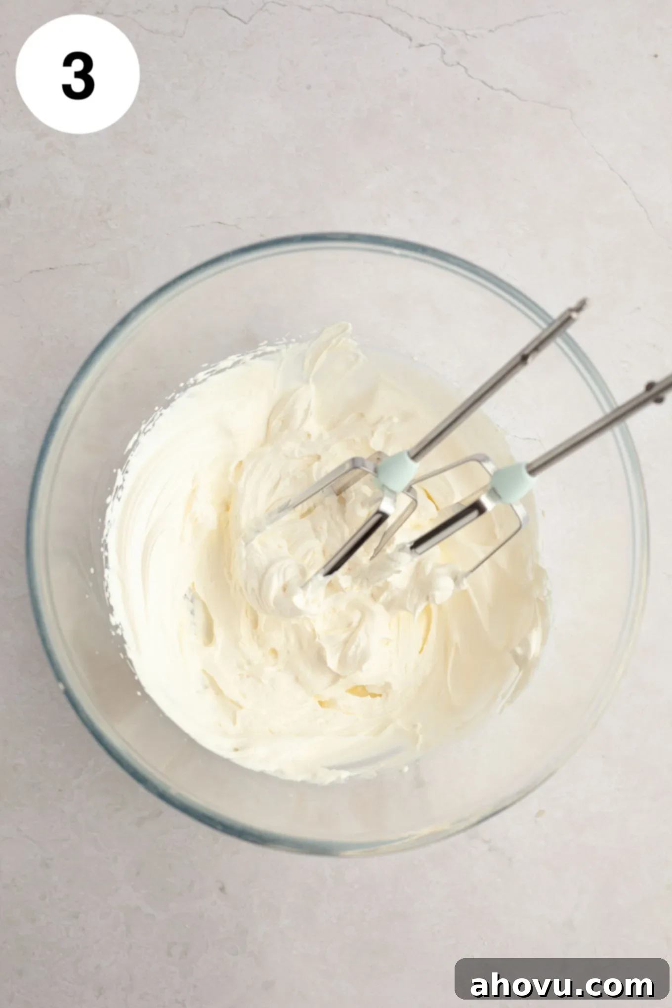 Strawberry Cheesecake Poppers 6 An overhead view of stiffly whipped heavy cream in a clear glass mixing bowl, with electric beaters resting beside it.