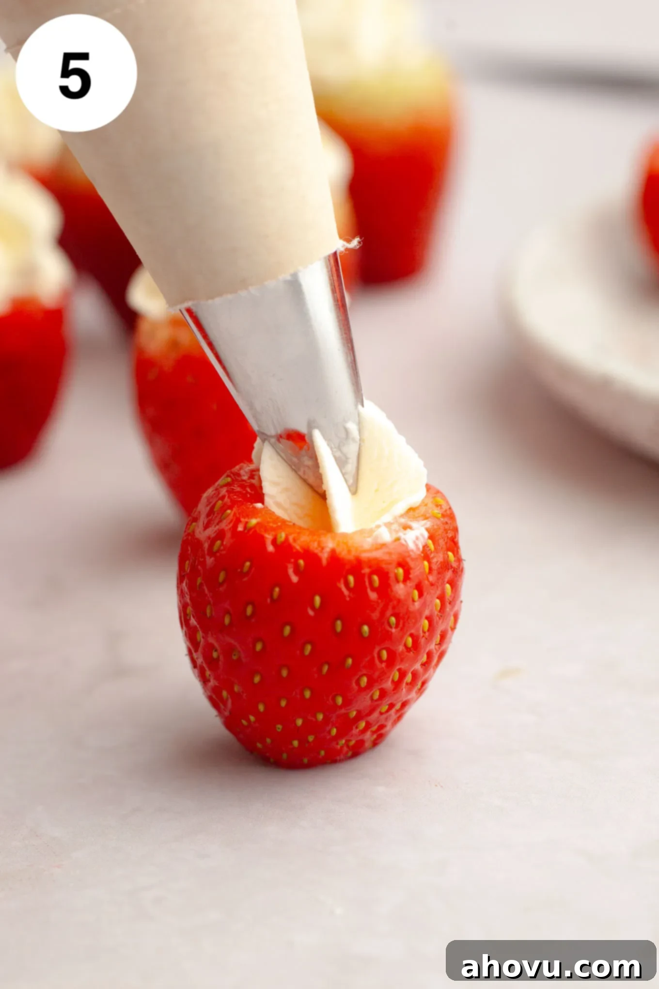 Strawberry Cheesecake Poppers 8 A process shot showing a fresh, hollowed-out strawberry being expertly filled with creamy cheesecake filling using a piping bag.
