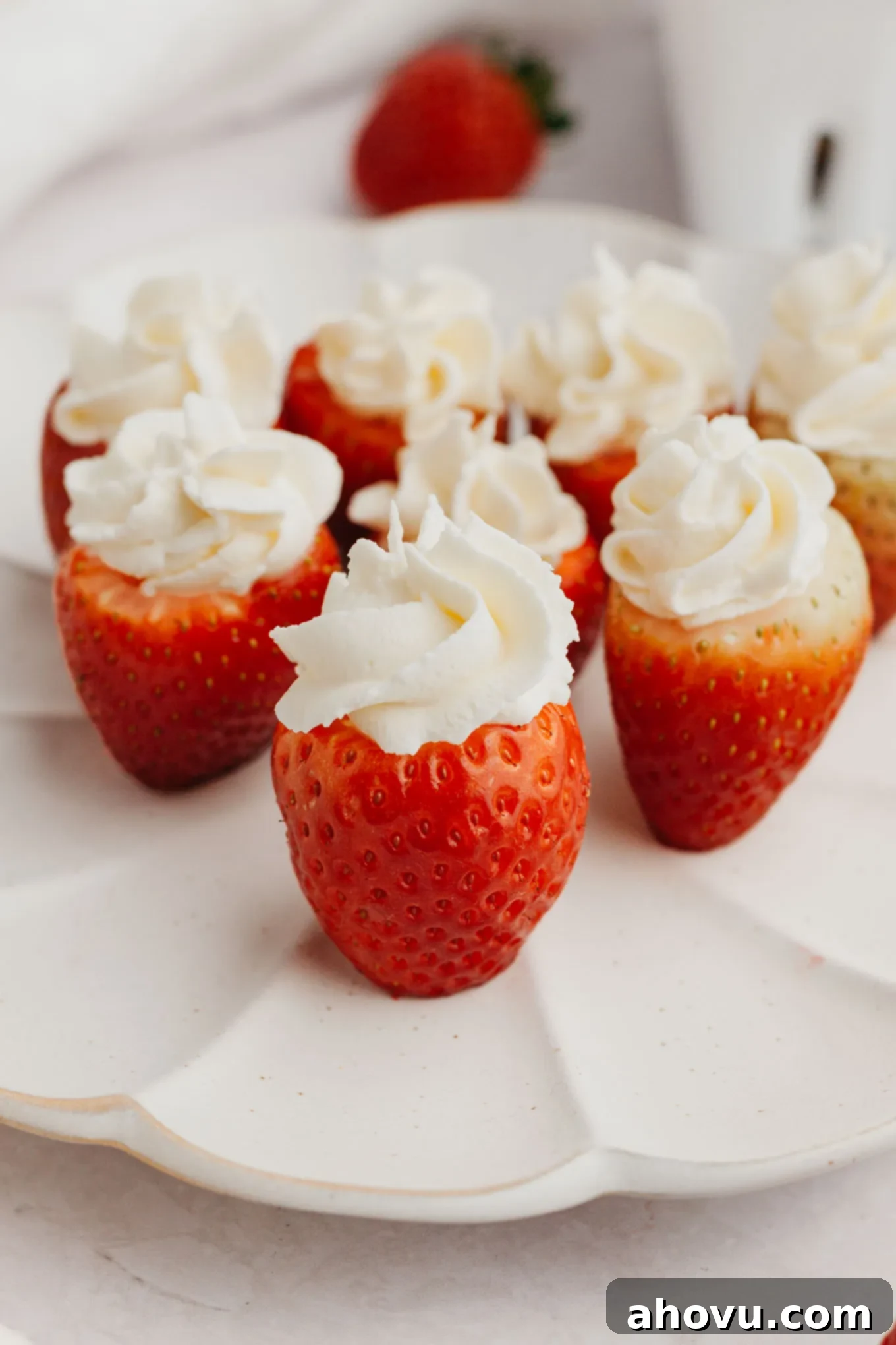 Strawberry Cheesecake Poppers 10 A close-up view of several elegantly piped cheesecake stuffed strawberries artfully arranged on a white plate, ready for serving.