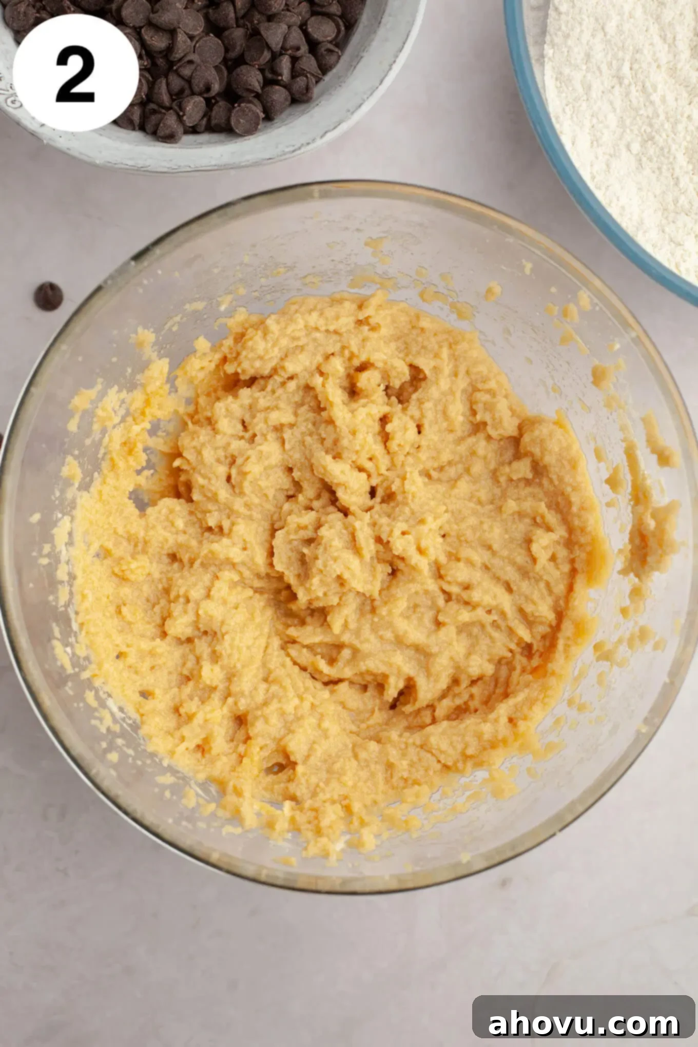An overhead view of a glass mixing bowl, showing the wet ingredients (creamed butter, cream cheese, sugars, egg, and vanilla) smoothly combined and ready for dry ingredients.