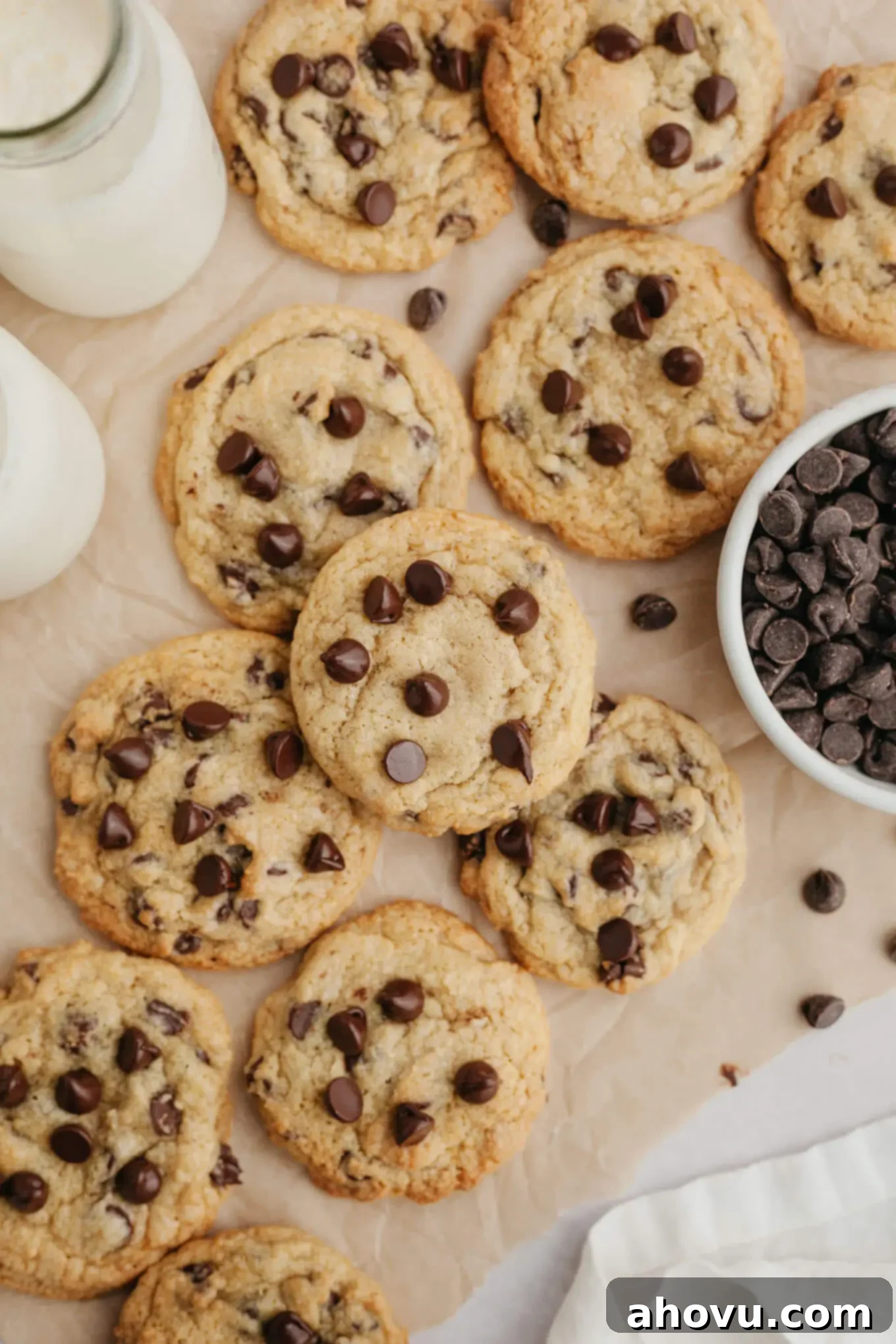 An overhead view of a batch of perfectly baked cream cheese chocolate chip cookies cooling on parchment paper, ready to be devoured.