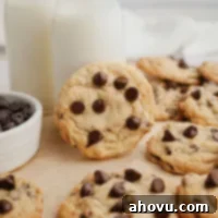 Several cream cheese chocolate chip cookies on a piece of brown parchment paper. One of the cookies is leaning against a glass of milk, inviting a delicious treat.