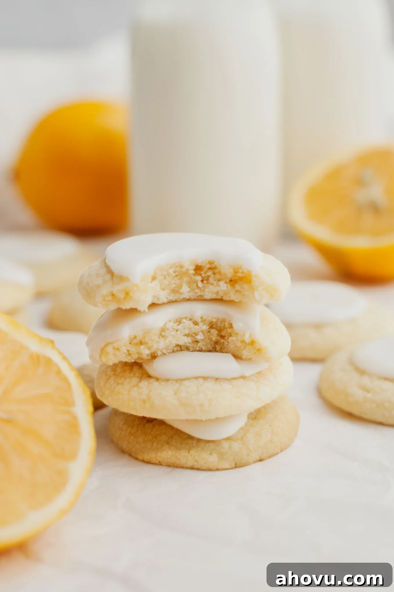 A stack of four lemon meltaways, surrounded by more cookies, showcasing their soft texture and bright glaze.