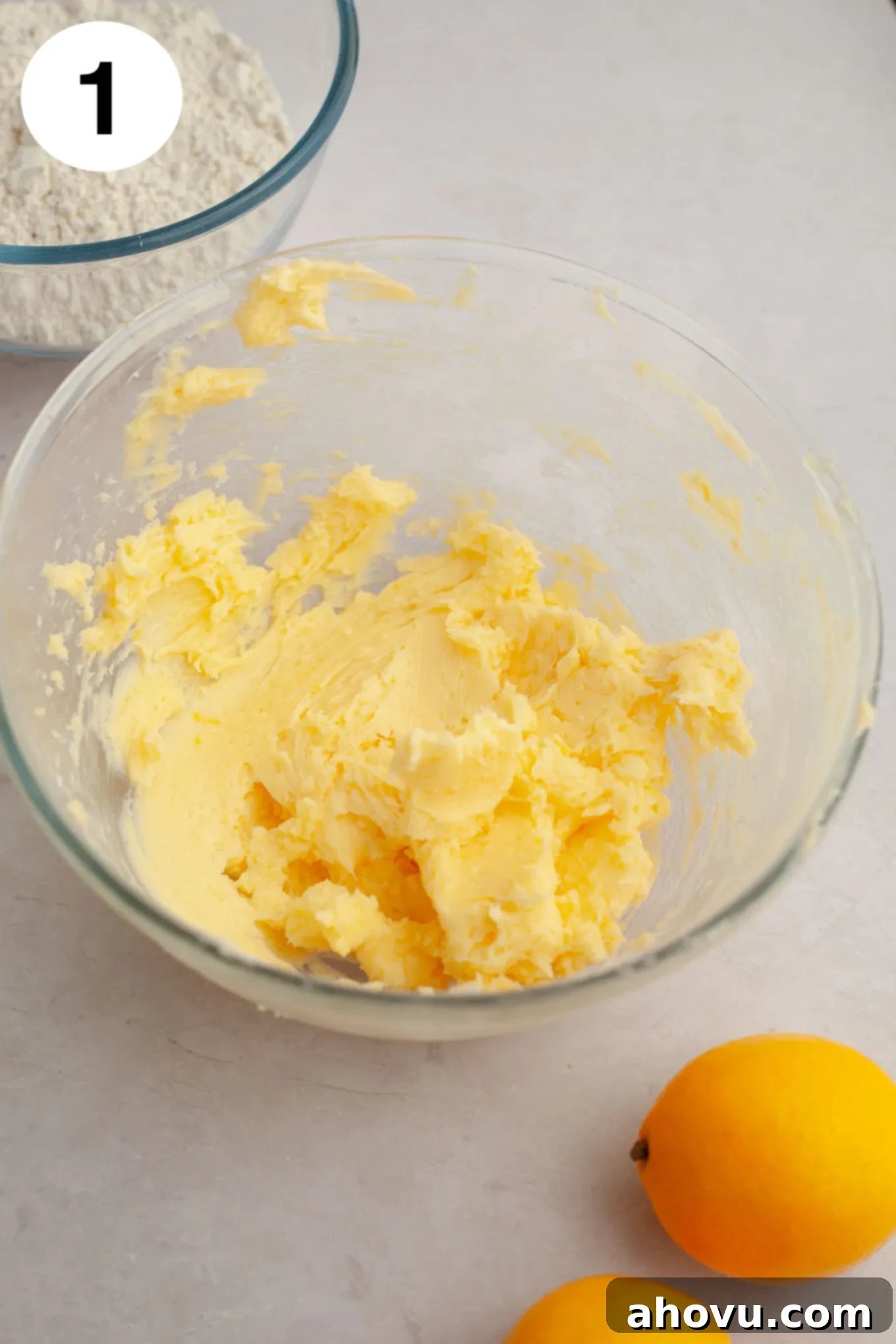 An overhead view of creamed butter, powdered sugar, egg yolk, and lemon zest and juice in a glass mixing bowl, ready to be combined.