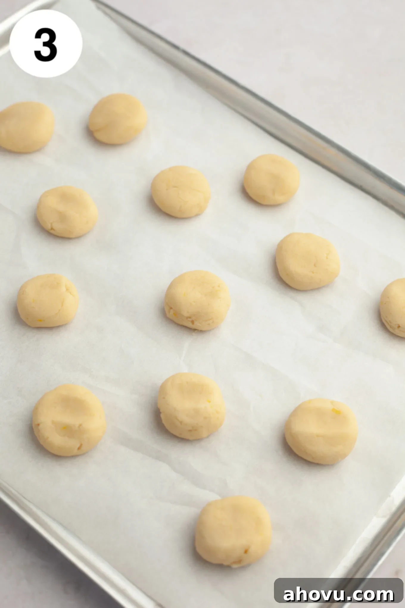 Unbaked lemon meltaway cookie dough balls, slightly flattened, arranged neatly on a parchment paper-lined baking sheet, ready for the oven.