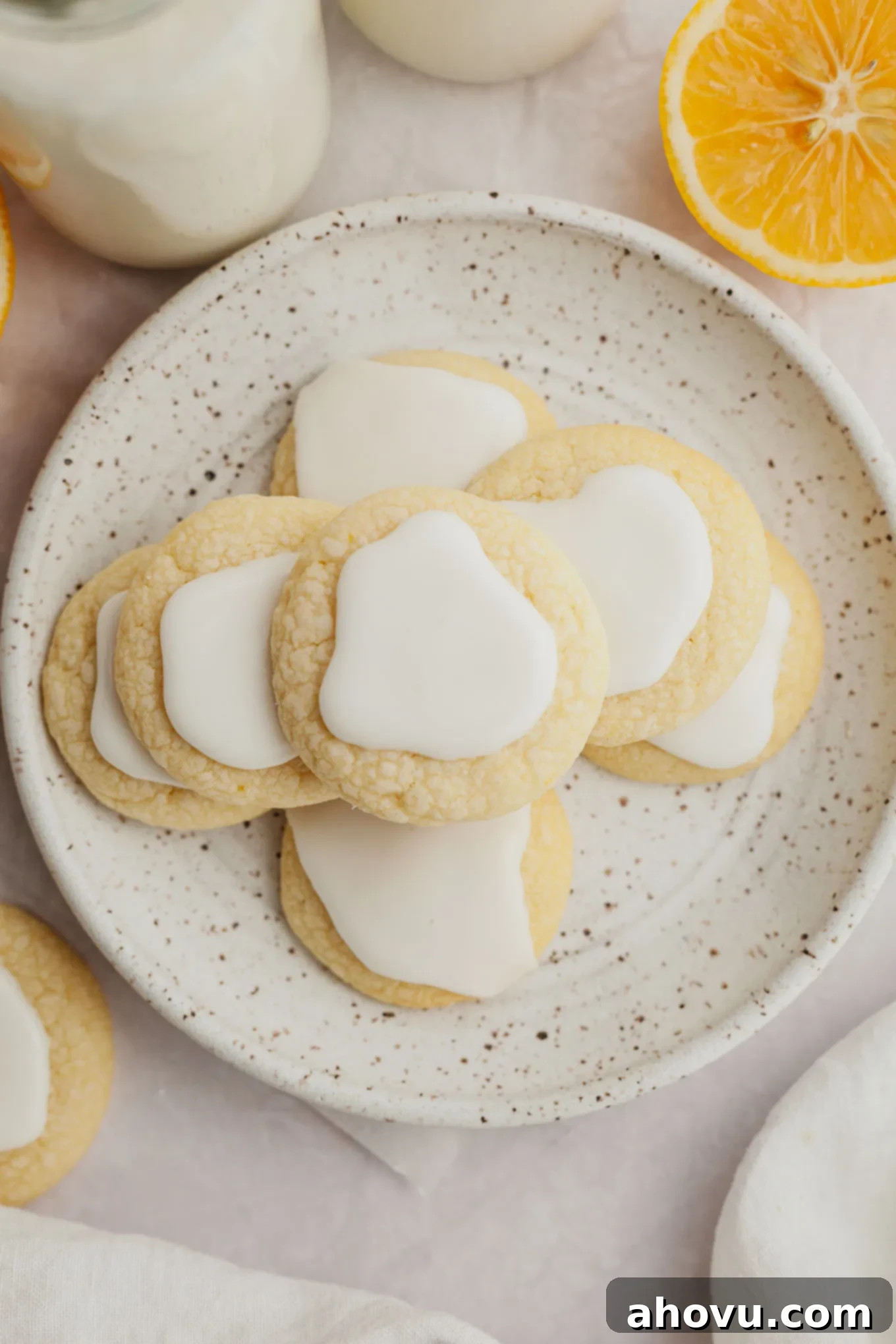 An overhead view of a perfectly arranged stack of lemon meltaway cookies with delicate icing, presented on a white speckled plate.