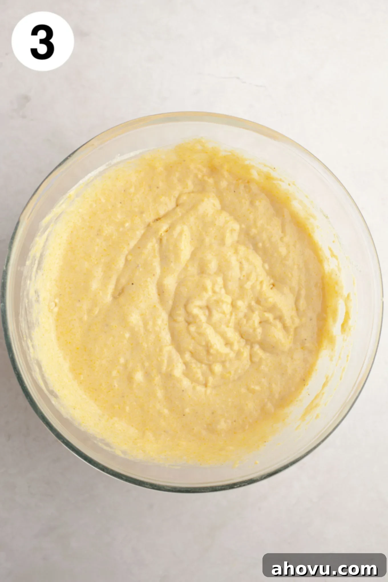 An overhead view of cornbread muffin batter in a glass mixing bowl.