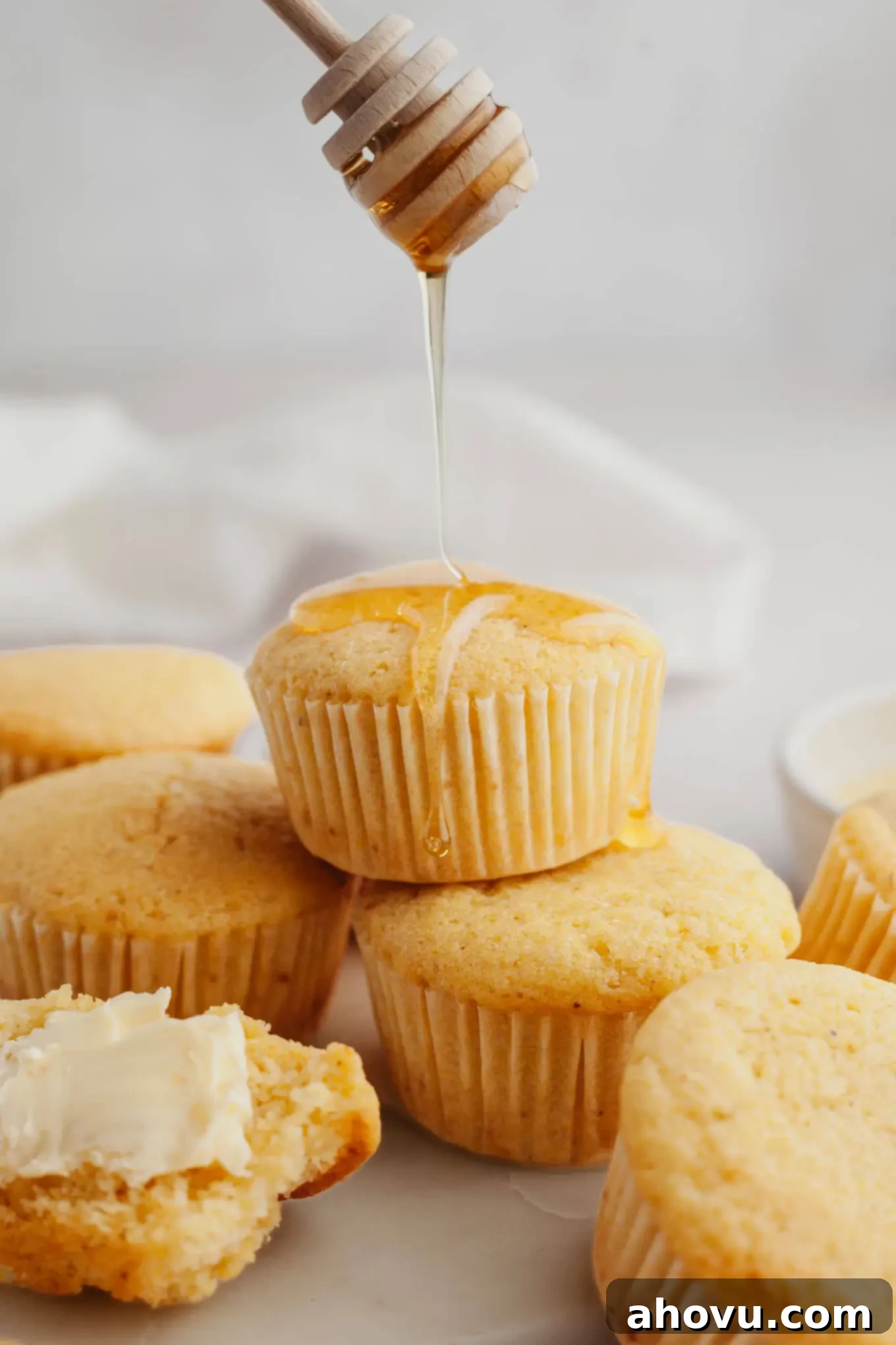An action shot showing honey being drizzled over a stack of sweet cornbread muffins. 