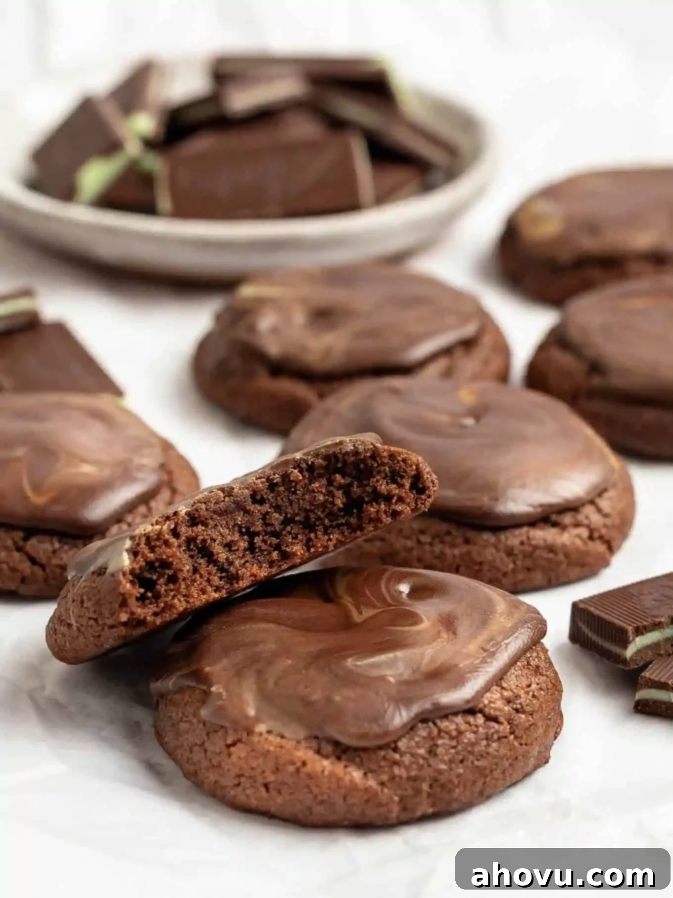 Several soft and chewy Andes mint cookies on a piece of white parchment paper, with a bowl of unwrapped Andes mints in the background, ready to be used or enjoyed.