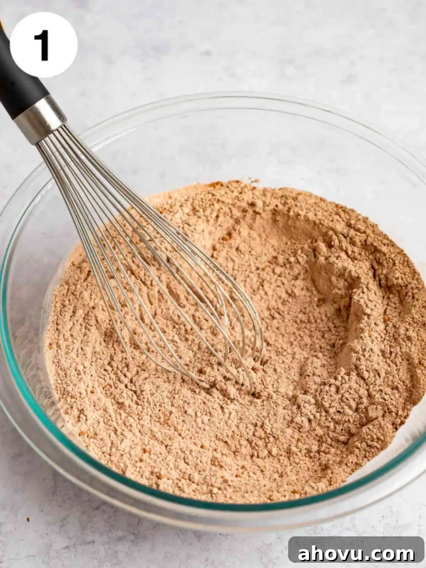 A glass mixing bowl containing all the dry ingredients, perfectly measured and whisked together, showing the rich color of cocoa powder.