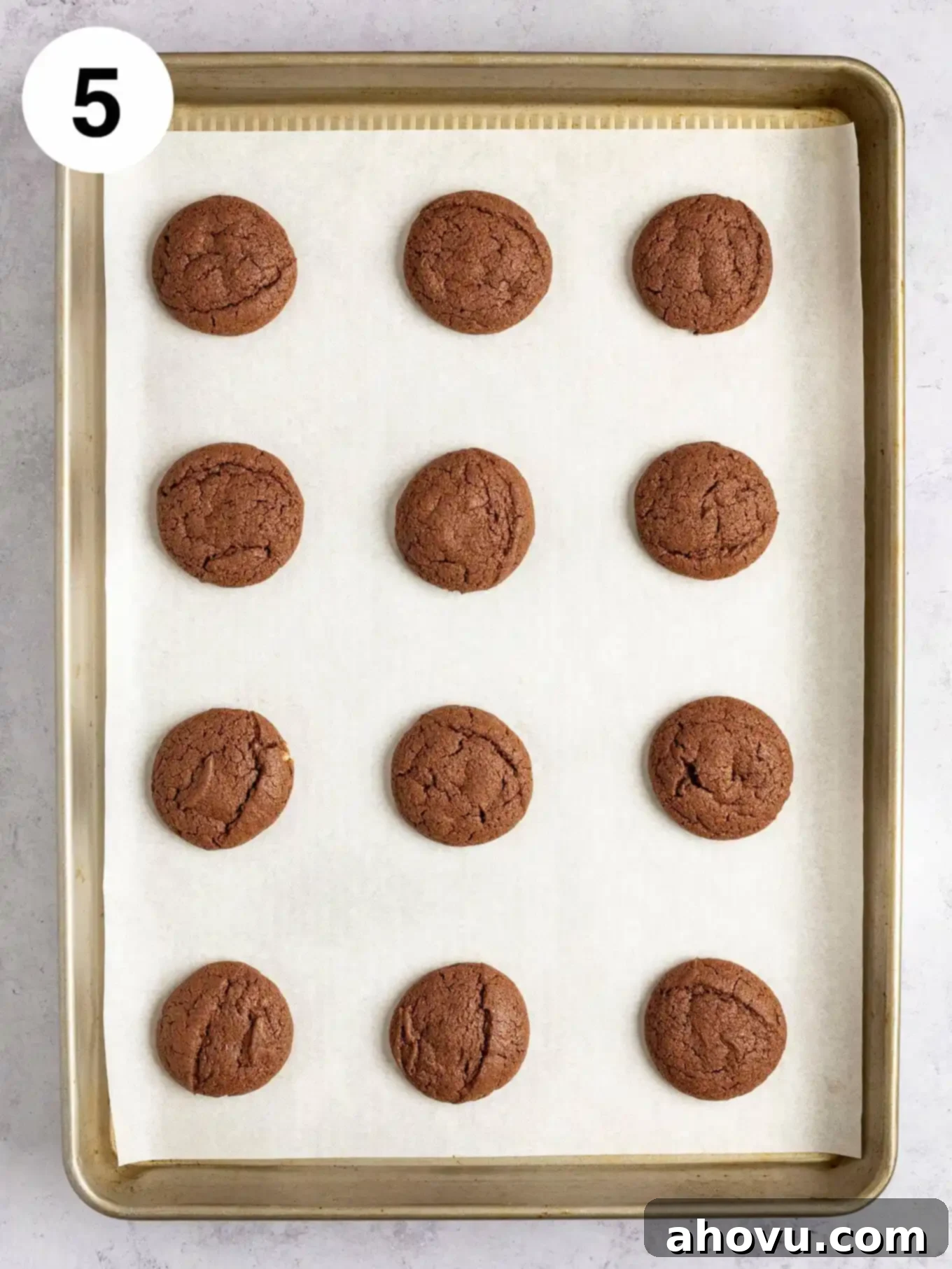 An overhead view of freshly baked chocolate cookies resting on a baking sheet lined with parchment paper, perfectly puffed and ready for the mint topping.