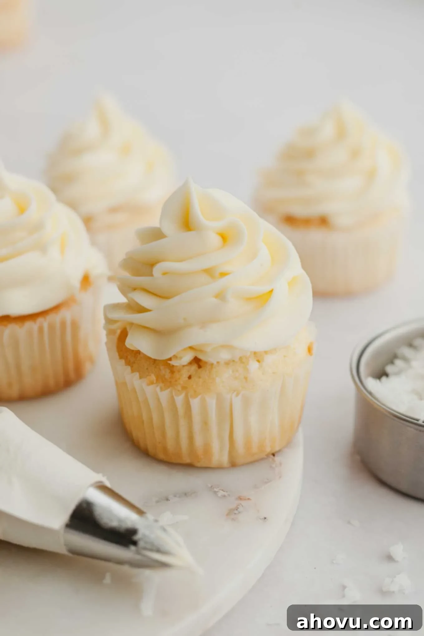 Several cupcakes generously topped with creamy coconut frosting, showcasing its smooth texture and inviting appearance.