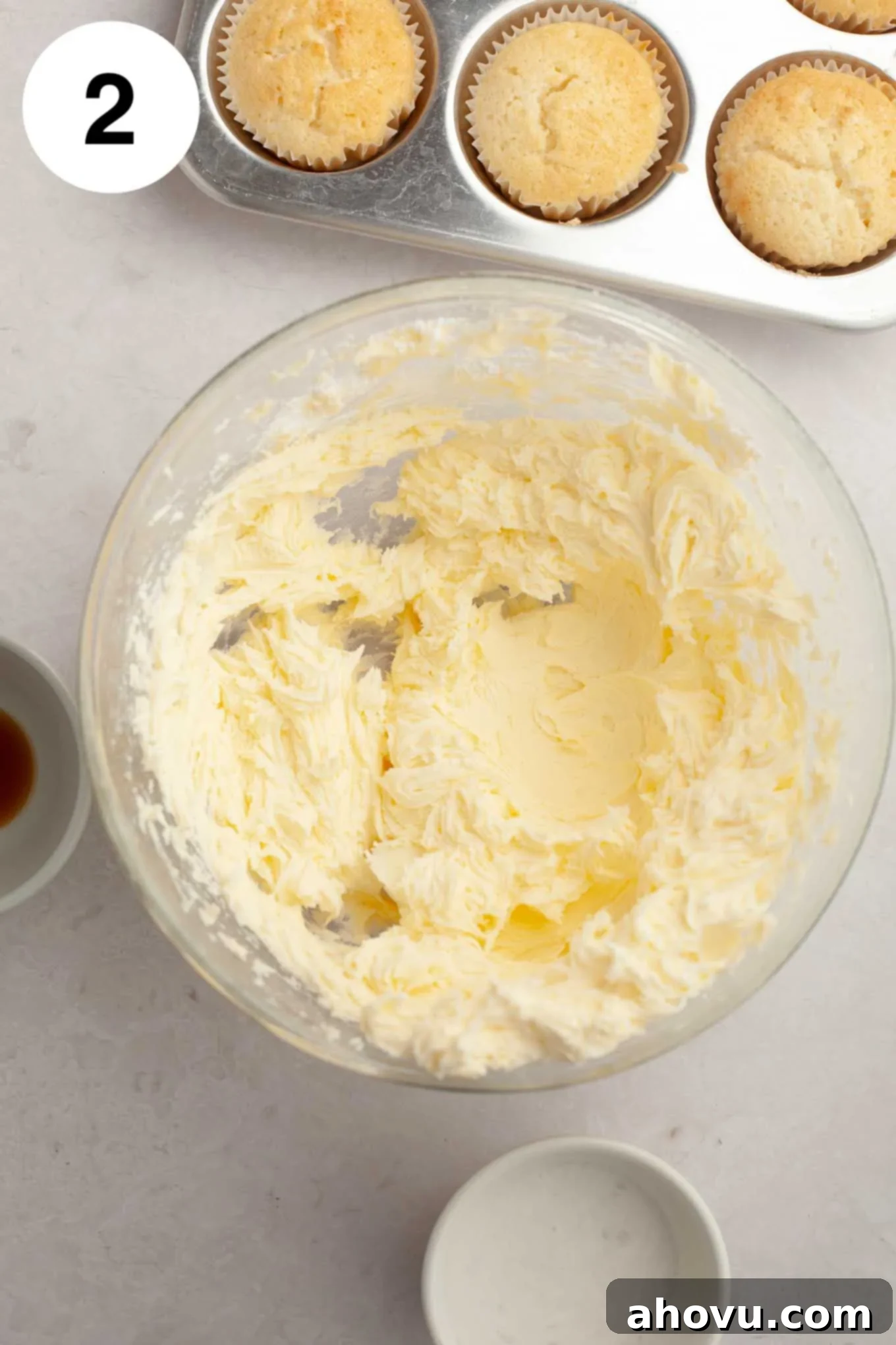 A close-up shot of butter and powdered sugar being thoroughly mixed together in a glass mixing bowl, creating a thick, uniform base.