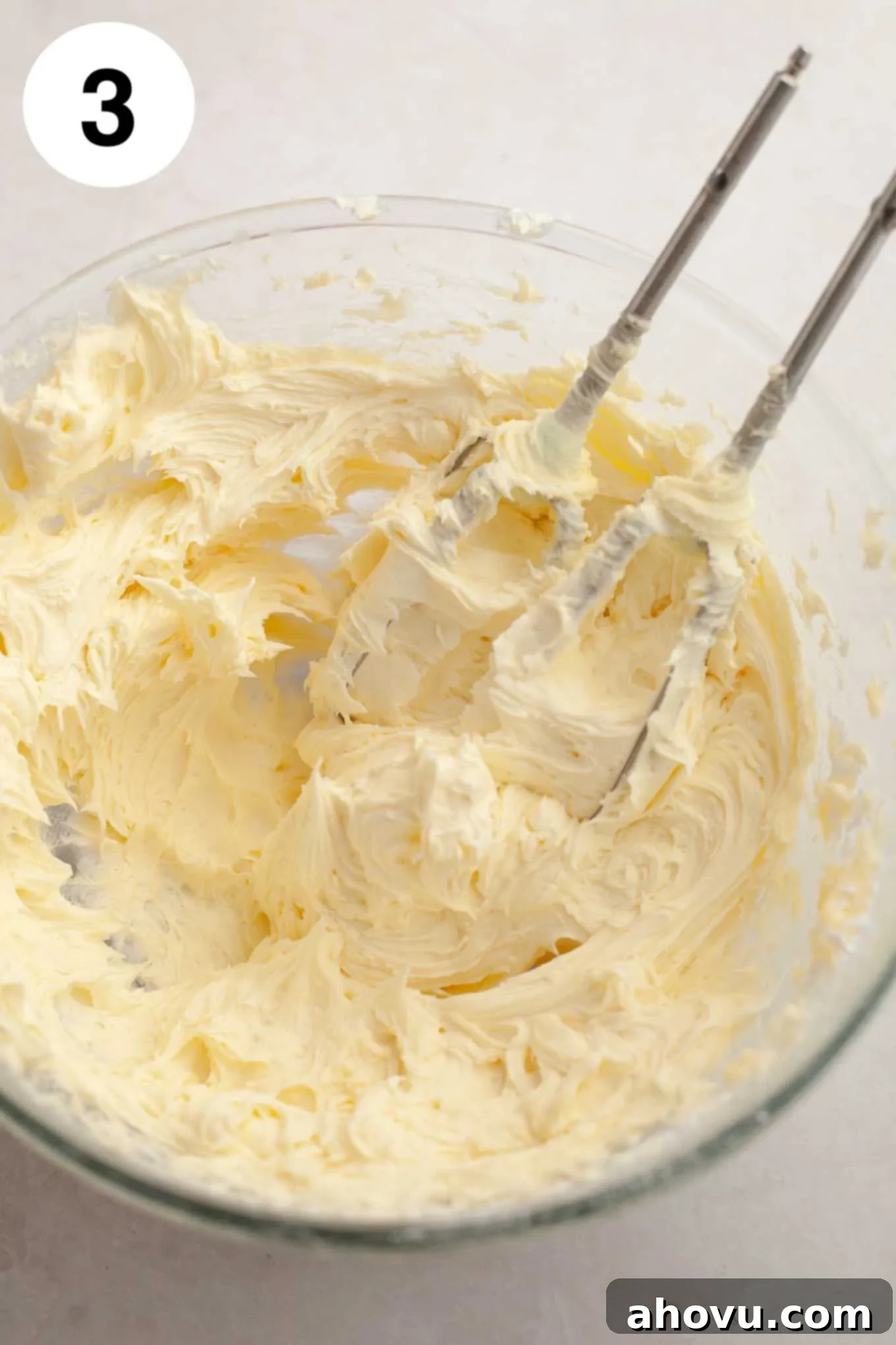 The fully mixed, creamy coconut frosting in a glass mixing bowl, showcasing its smooth texture and readiness for use.